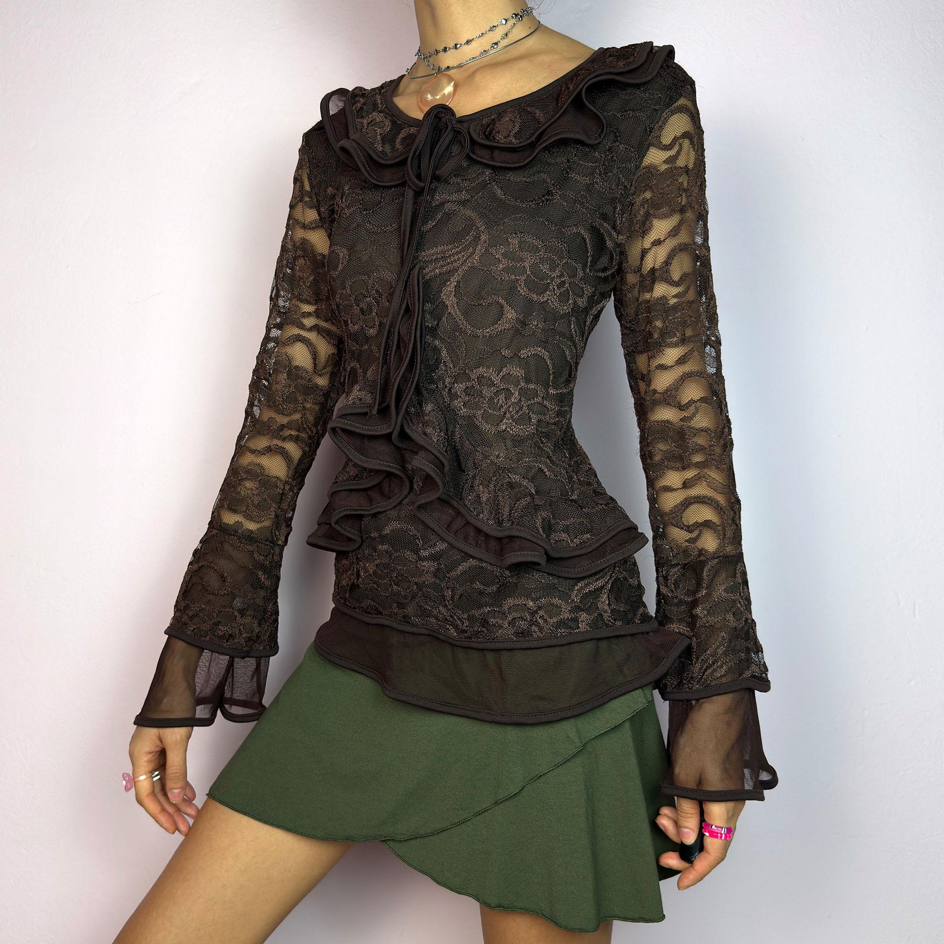 The Y2K Brown Lace Ruffle Top is a vintage 2000s statement piece, showcasing intricate floral lace throughout for a romantic and feminine look. This top features a stretchy semi-sheer fabric, layered ruffles along the neckline. adult world shop