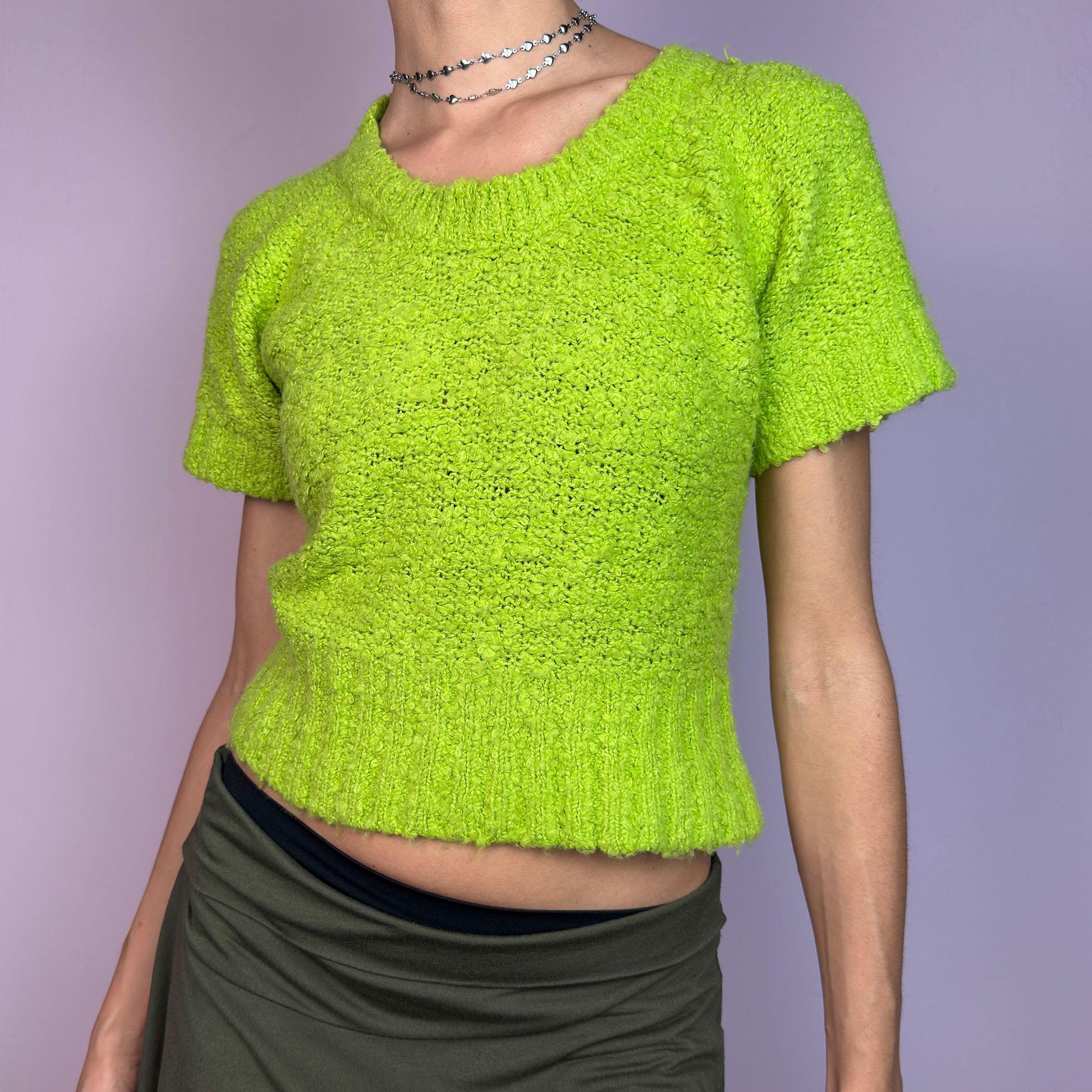 The Y2K Green Knitted Top is a vibrant vintage 2000s piece featuring a lime-green hue. Designed with a cropped silhouette, short sleeves, and a stretchy ribbed hem, this knit top adds a playful touch to casual outfits. adult world shop