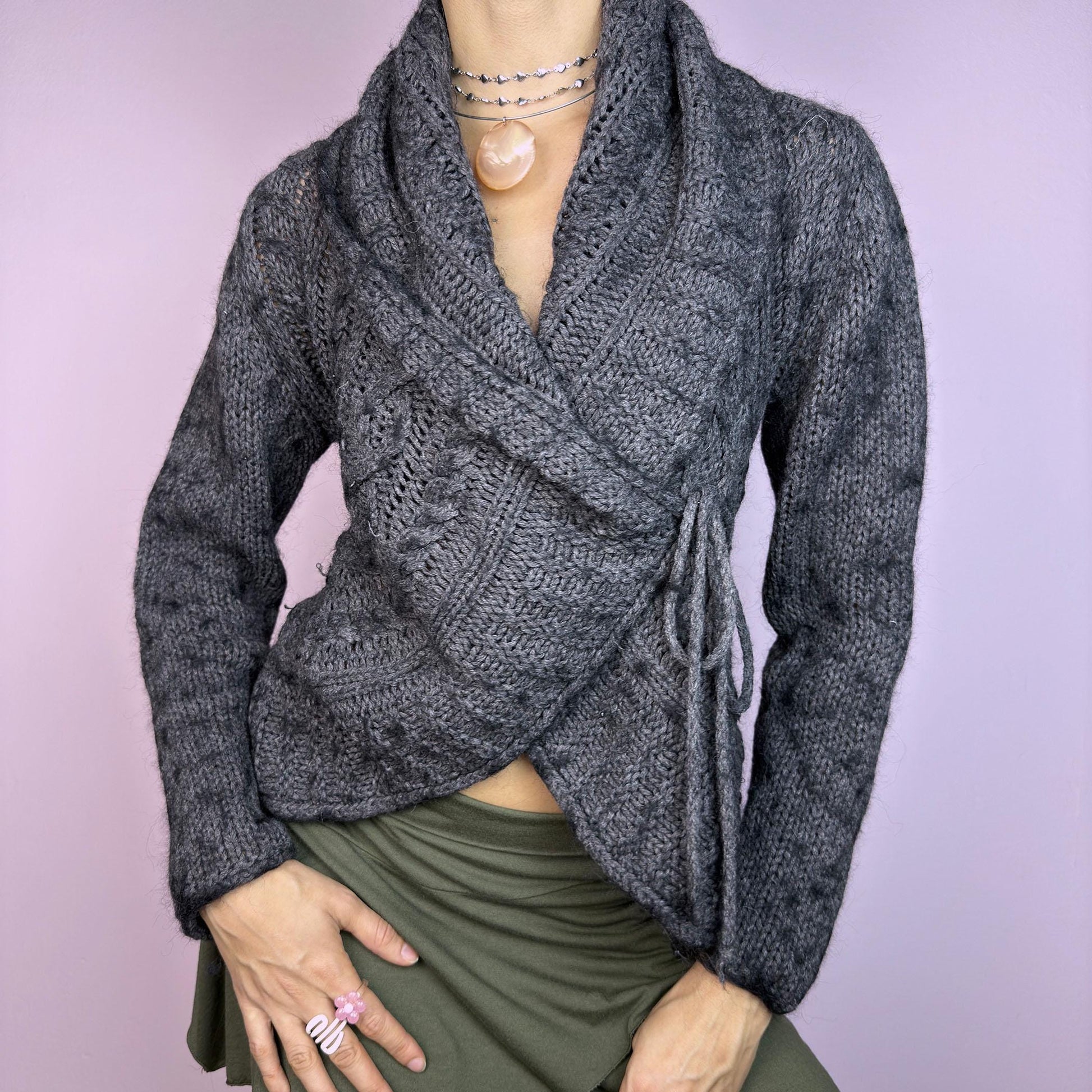 The Y2K Gray Wrap Tie Cardigan is a cozy vintage 2000s piece. This dark gray cardigan features a chunky knit design with intricate cable-knit detailing and a wrap-front closure that ties at the side for an adjustable fit. adult world shop