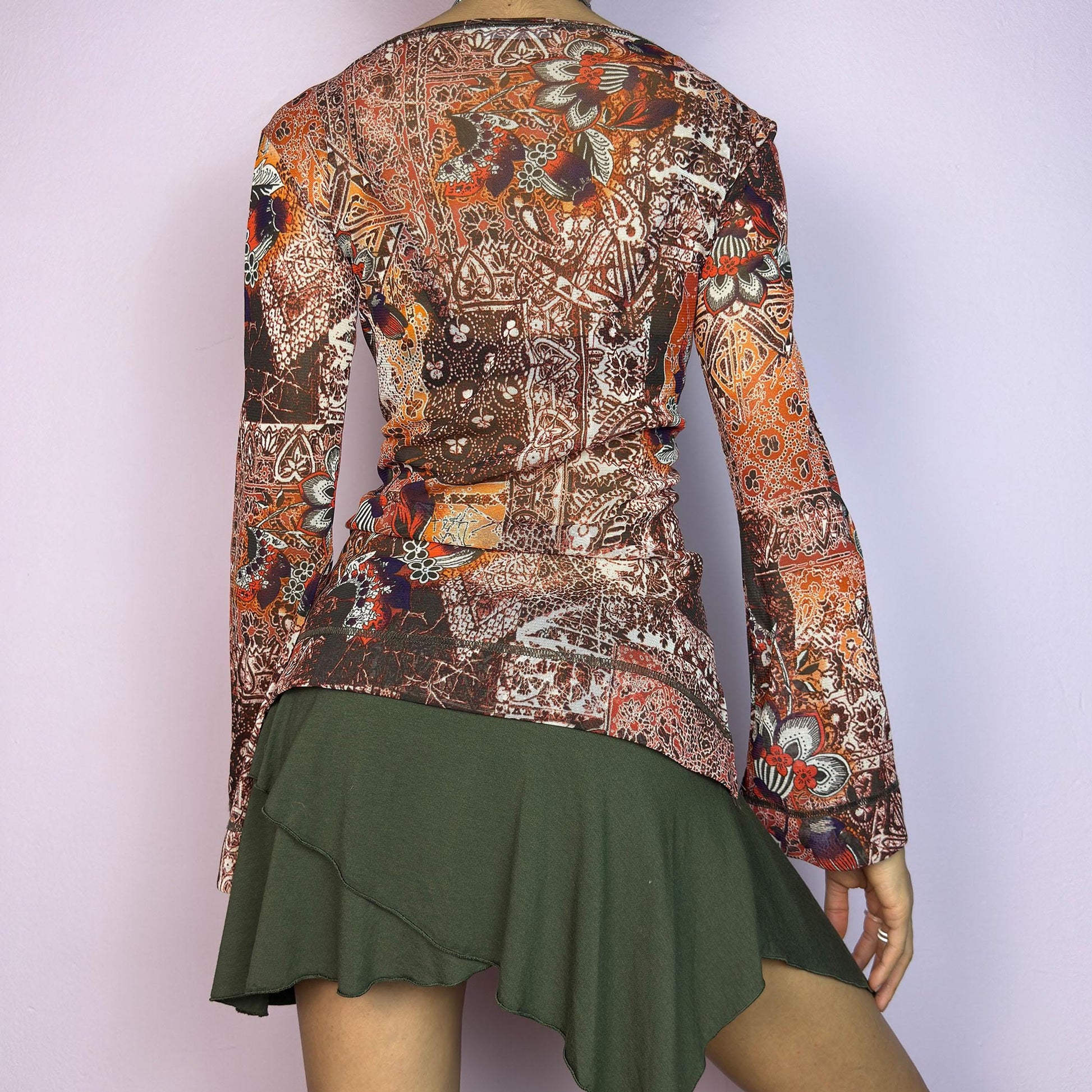 The Y2K Mesh Flared Long Sleeve Top is a vibrant vintage 2000s piece, featuring a floral and paisley print in earthy tones of orange, red, and brown. Crafted from lightweight mesh fabric, this top has a semi-sheer finish. adult world shop