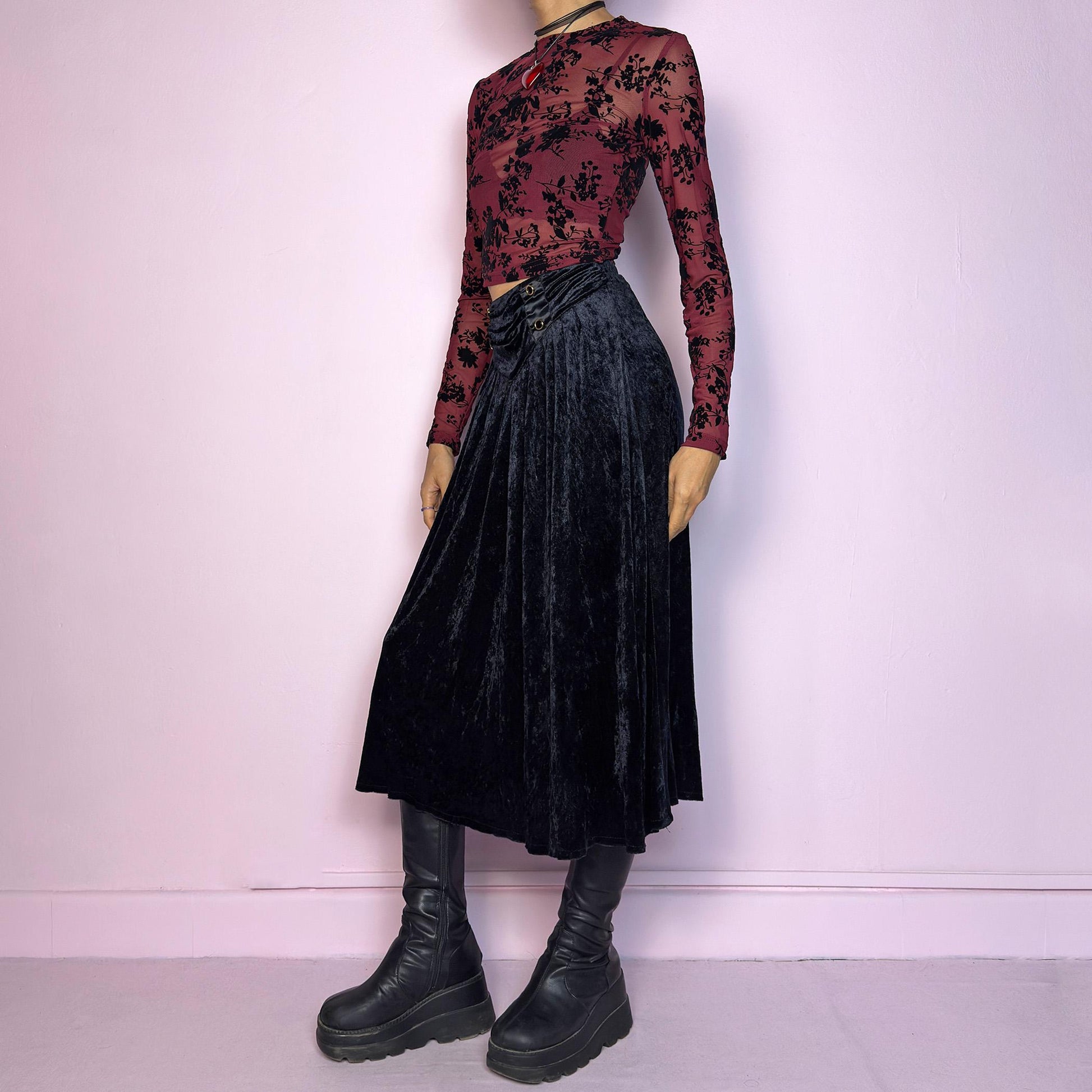 The Vintage 90s Black Velvet Midi Skirt is crafted from soft velvet and features an elastic waistband detail with button accents and a flowing A-line silhouette. Ideal for night parties and embodies a whimsical goth aesthetic. Adult World Shop