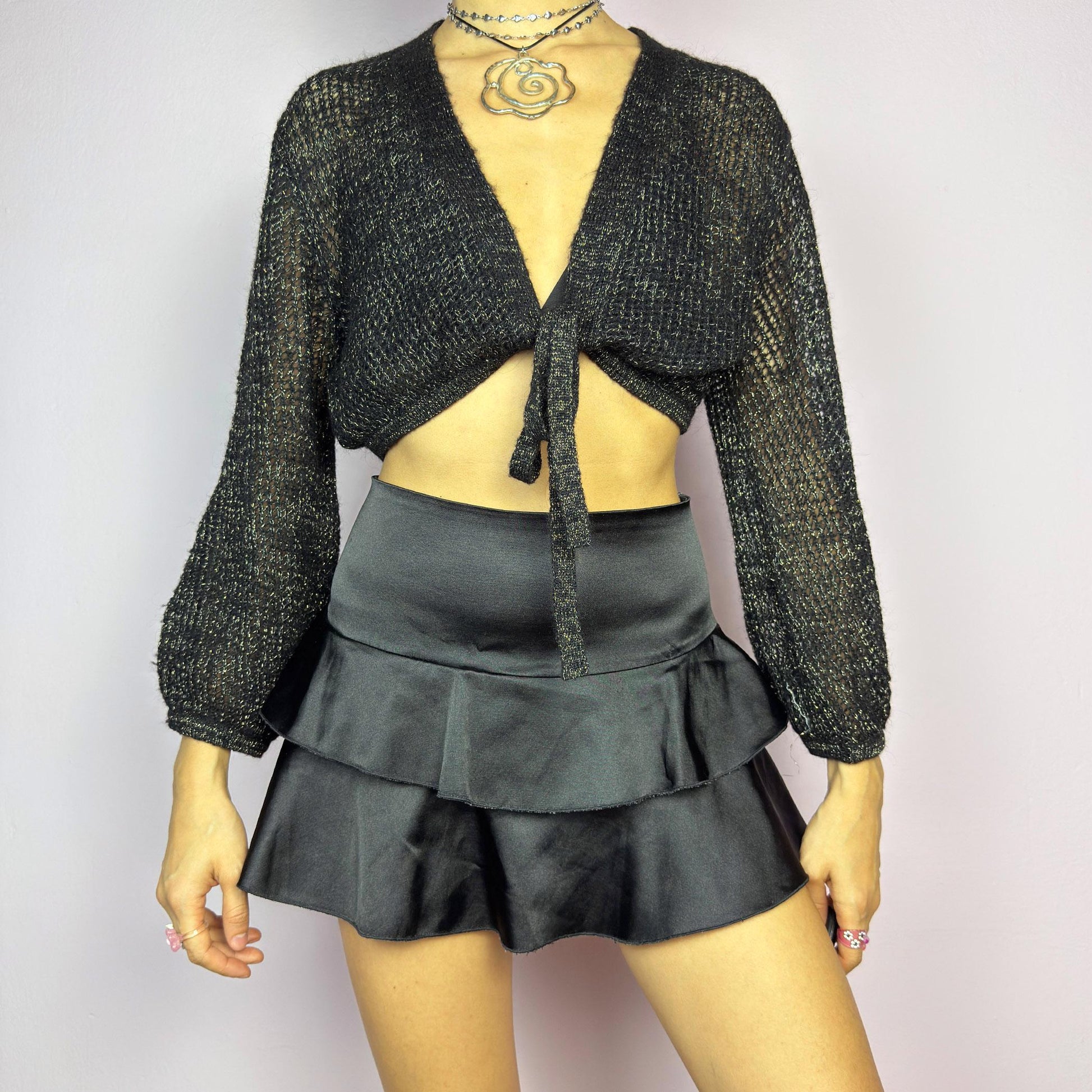 This Y2K Black Tie Front Cardigan is a vintage 2000s piece featuring a lightweight open-knit design with a subtle metallic shimmer, a cropped fit and long sleeves. Perfect for layering and ideal for night-out or casual outfits.
