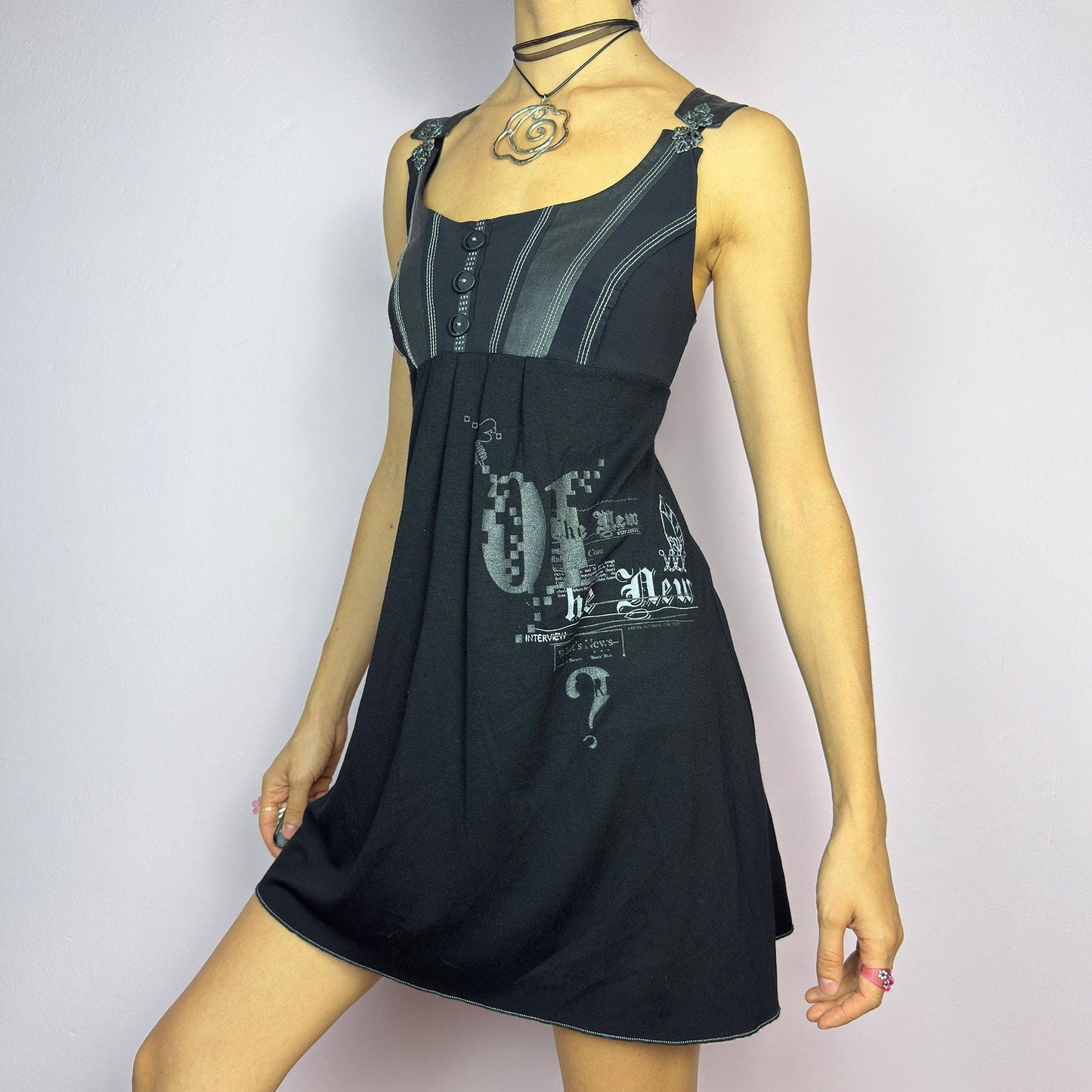 The Y2K Black Buckle Strap Mini Dress is a vintage 2000s sleeveless piece with a mix of edgy and casual aesthetics. It features decorative button details, contrast stitching, and graphic prints. adult world shop
