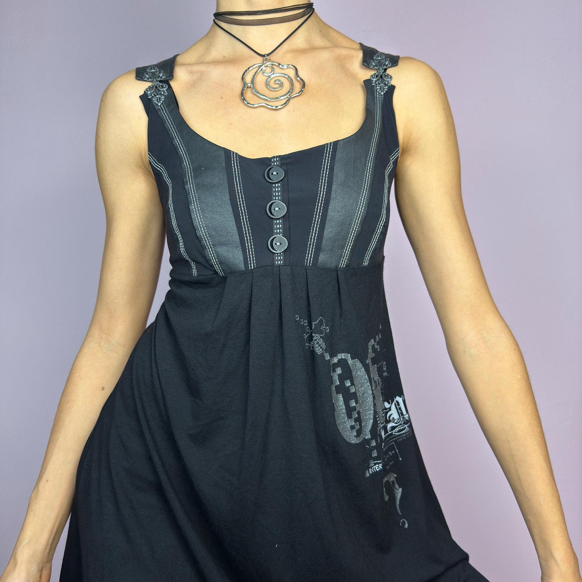 The Y2K Black Buckle Strap Mini Dress is a vintage 2000s sleeveless piece with a mix of edgy and casual aesthetics. It features decorative button details, contrast stitching, and graphic prints. adult world shop