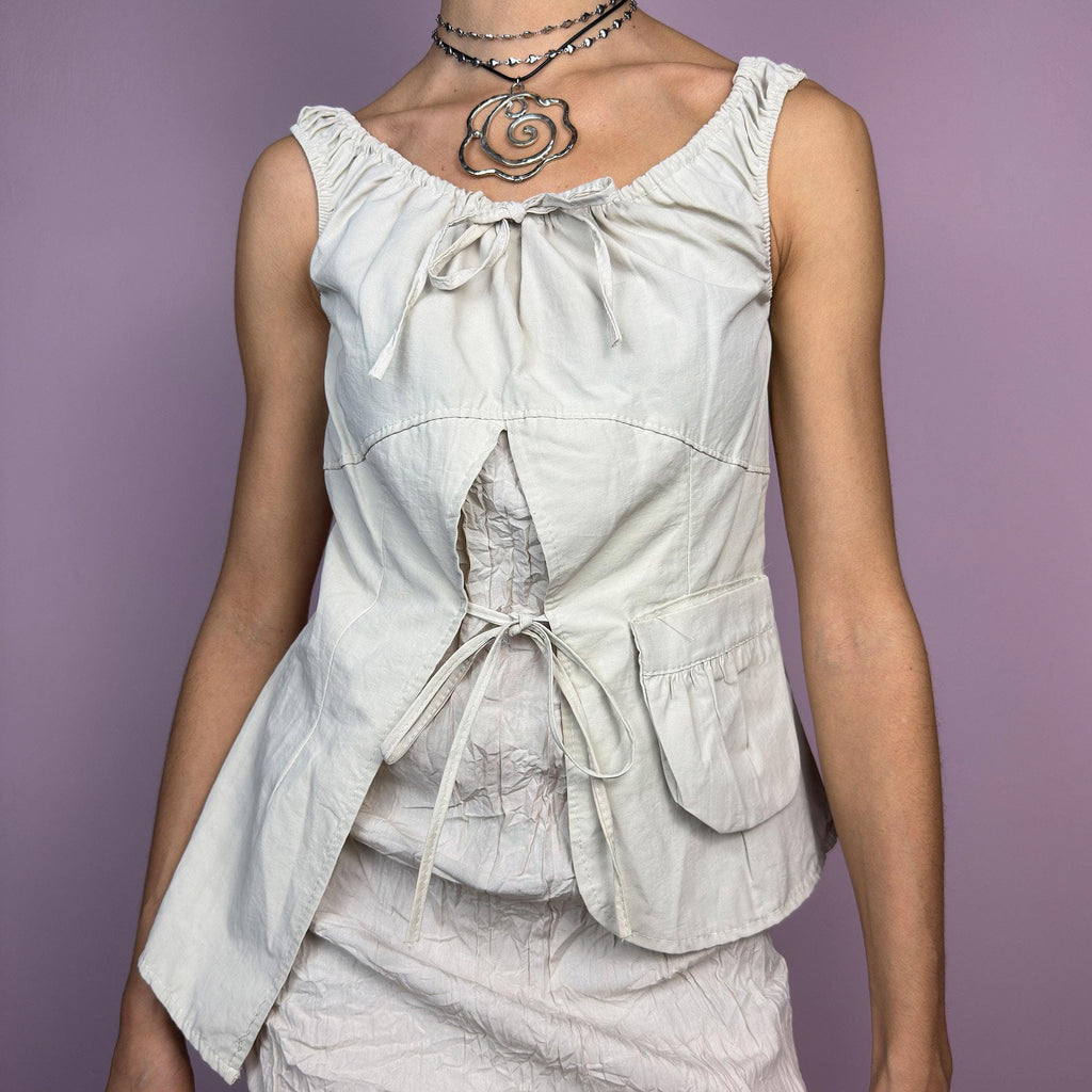 The Y2K Cream Asymmetric Tie Top is a vintage 2000s piece with a deconstructed aesthetic, featuring an asymmetric cut with a ruched neckline and delicate tie detail. The split front with adjustable ties creates a layered effect. adult world shop
