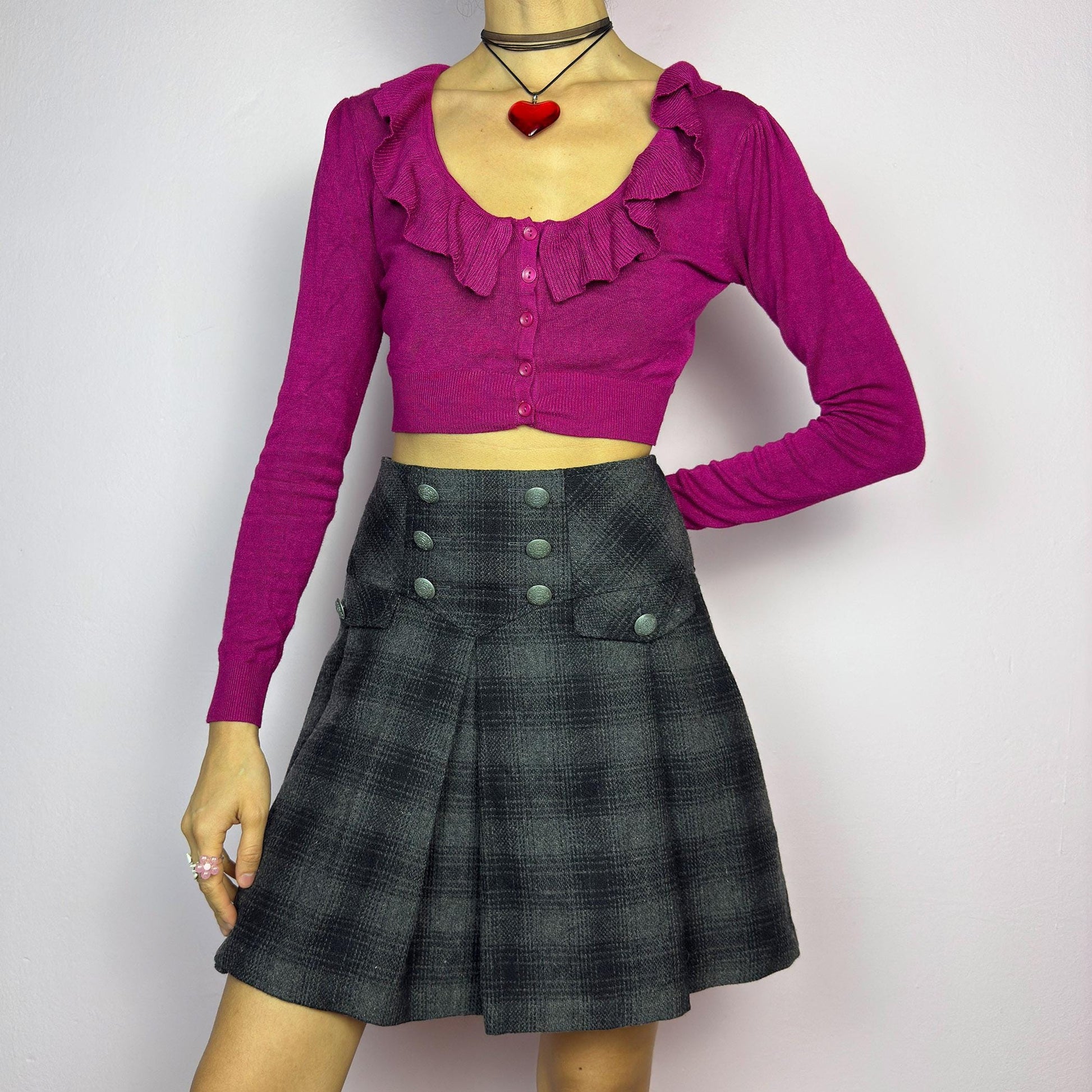 The Y2K Gray Plaid Pleated Mini Skirt is a vintage 2000s essential, featuring a structured pleated design with decorative button details. Made from a thick woven fabric with a black plaid pattern, it is ideal for winter outfits. adult world shop