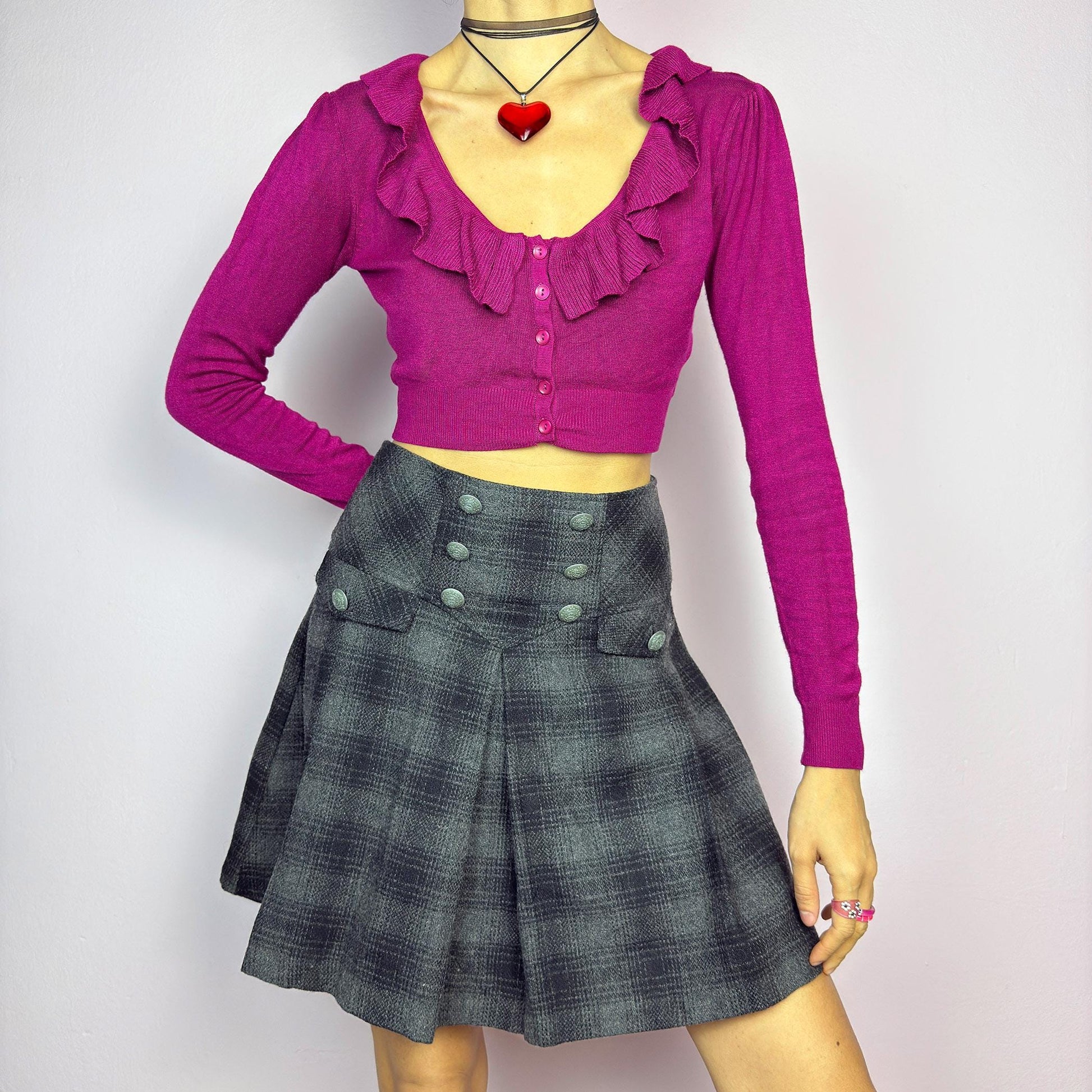 The Y2K Gray Plaid Pleated Mini Skirt is a vintage 2000s essential, featuring a structured pleated design with decorative button details. Made from a thick woven fabric with a black plaid pattern, it is ideal for winter outfits. adult world shop