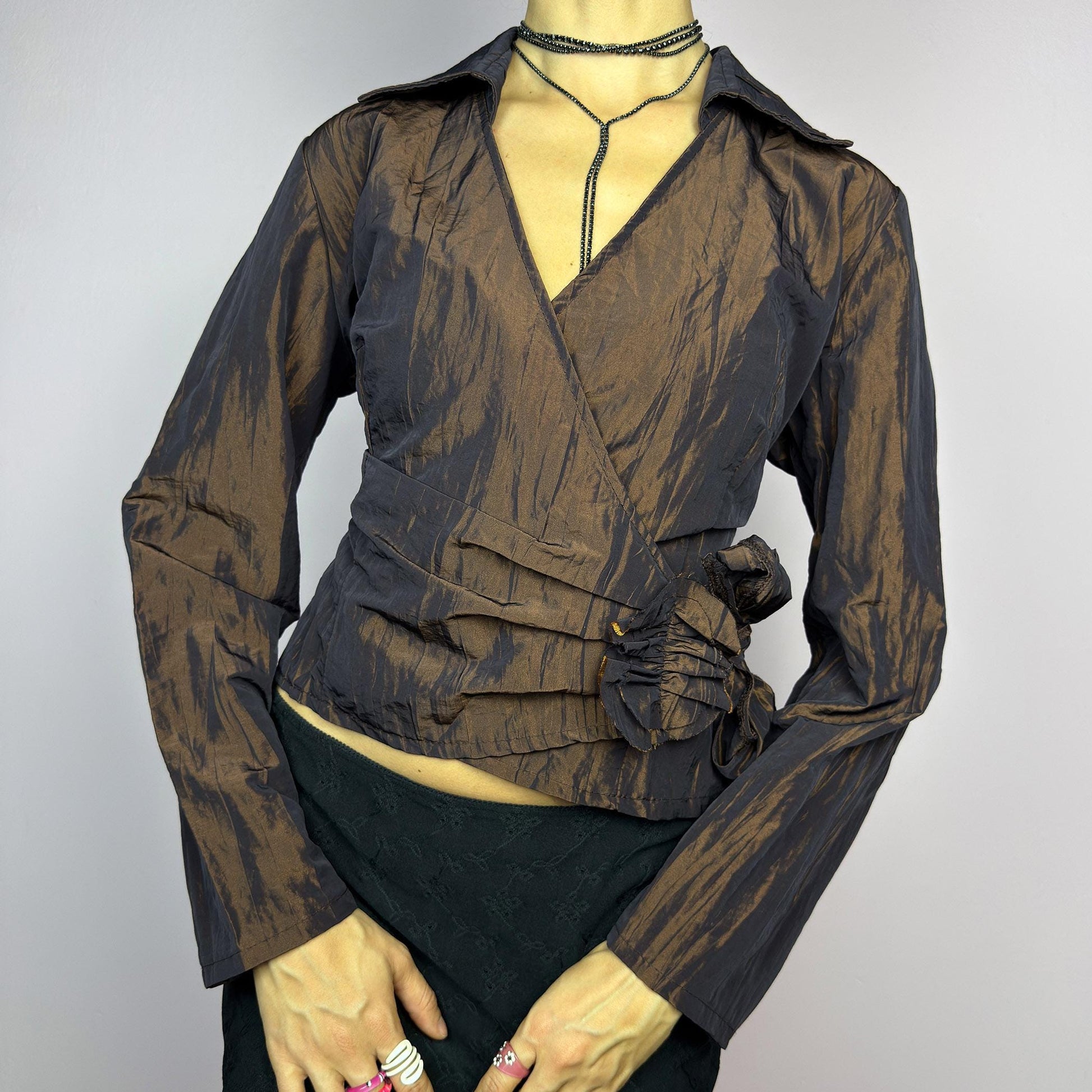 The Vintage 90s Brown Wrap Tie Blouse features a textured, crinkled fabric with a subtle iridescent finish, a flattering wrap design with a tie at the side. The deep brown tone adds versatility, while the structured collar. adult world shop