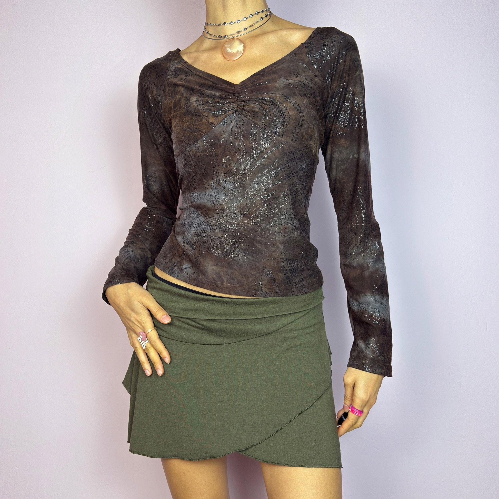 The Y2K Brown Earthy Shimmer Top is a vintage 2000s fitted and stretchy long-sleeve blouse with an earthy, abstract pattern featuring a ruched detail at the bust and subtle shimmering accents throughout. Perfect for casual outings. adult world shop