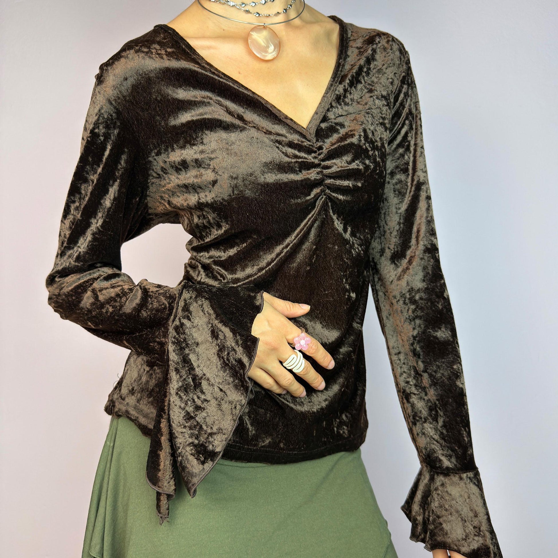 The Vintage 90s Brown Velvet Top is an elegant piece crafted from soft, stretchy velvet fabric. It features a rich chocolate brown hue, a flattering V-neckline with ruching detail at the bust, and dramatic bell sleeves. adult world shop