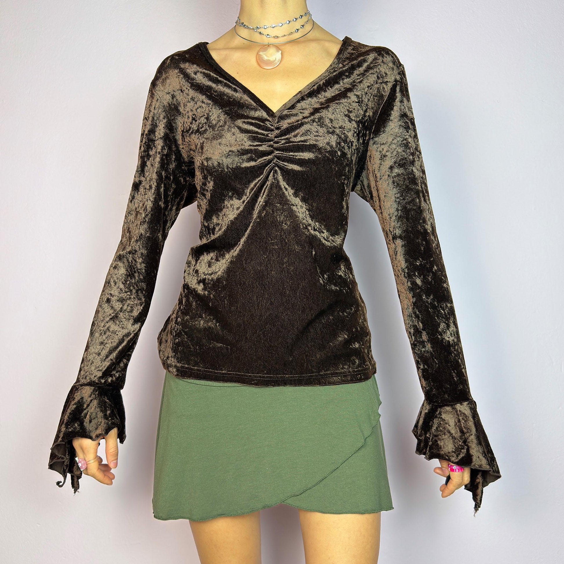 The Vintage 90s Brown Velvet Top is an elegant piece crafted from soft, stretchy velvet fabric. It features a rich chocolate brown hue, a flattering V-neckline with ruching detail at the bust, and dramatic bell sleeves. adult world shop