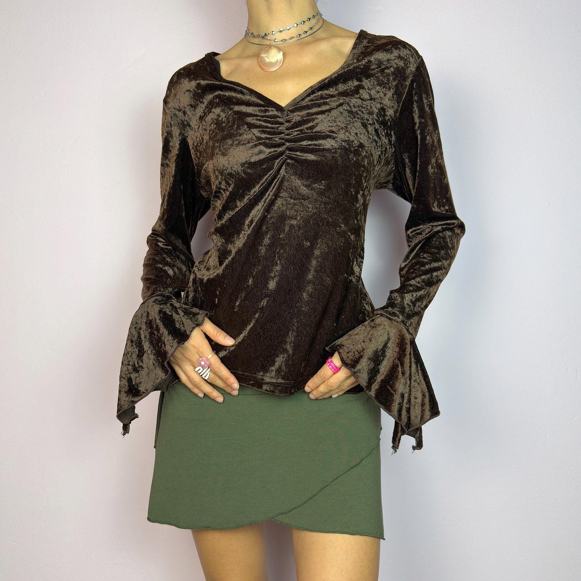 The Vintage 90s Brown Velvet Top is an elegant piece crafted from soft, stretchy velvet fabric. It features a rich chocolate brown hue, a flattering V-neckline with ruching detail at the bust, and dramatic bell sleeves. adult world shop