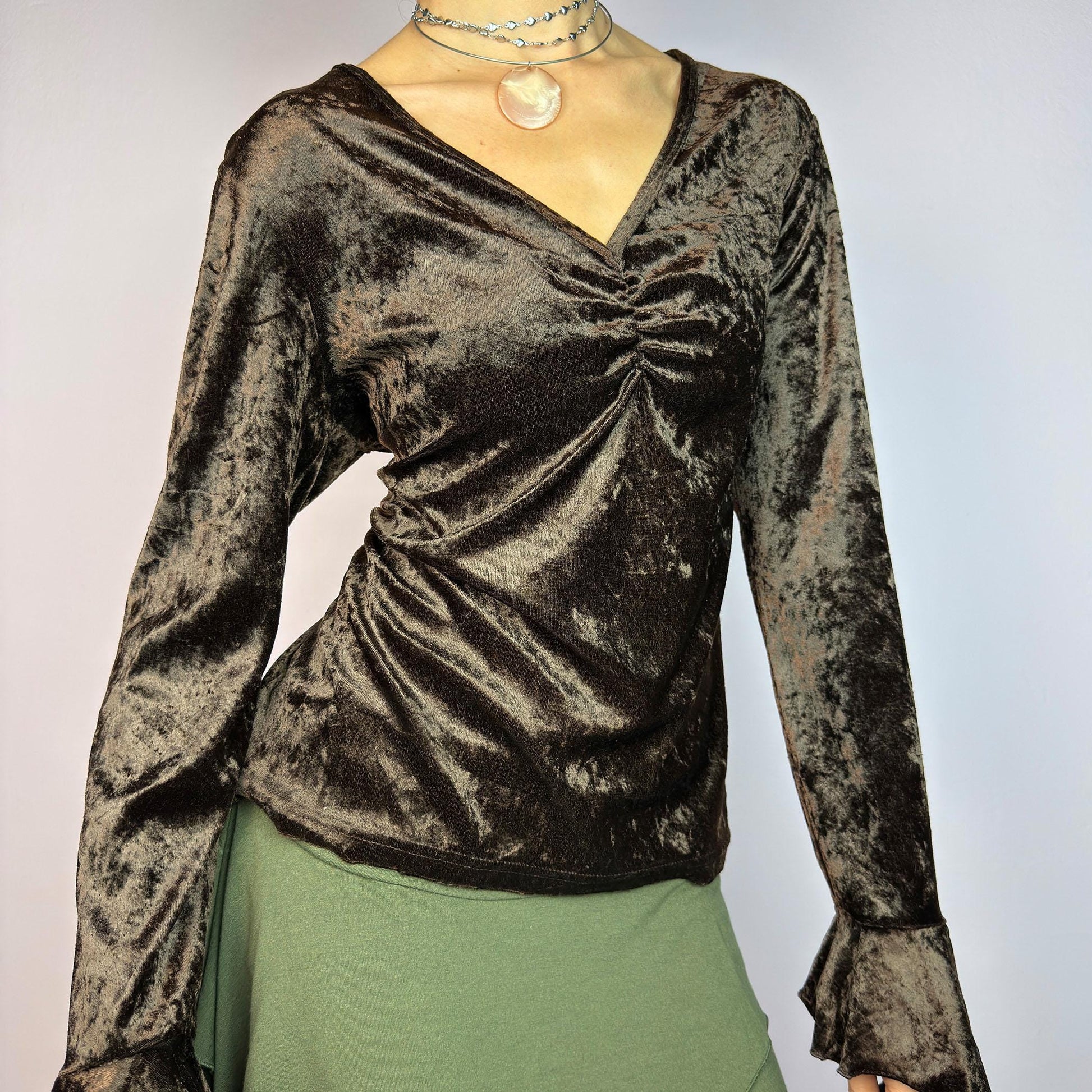 The Vintage 90s Brown Velvet Top is an elegant piece crafted from soft, stretchy velvet fabric. It features a rich chocolate brown hue, a flattering V-neckline with ruching detail at the bust, and dramatic bell sleeves. adult world shop