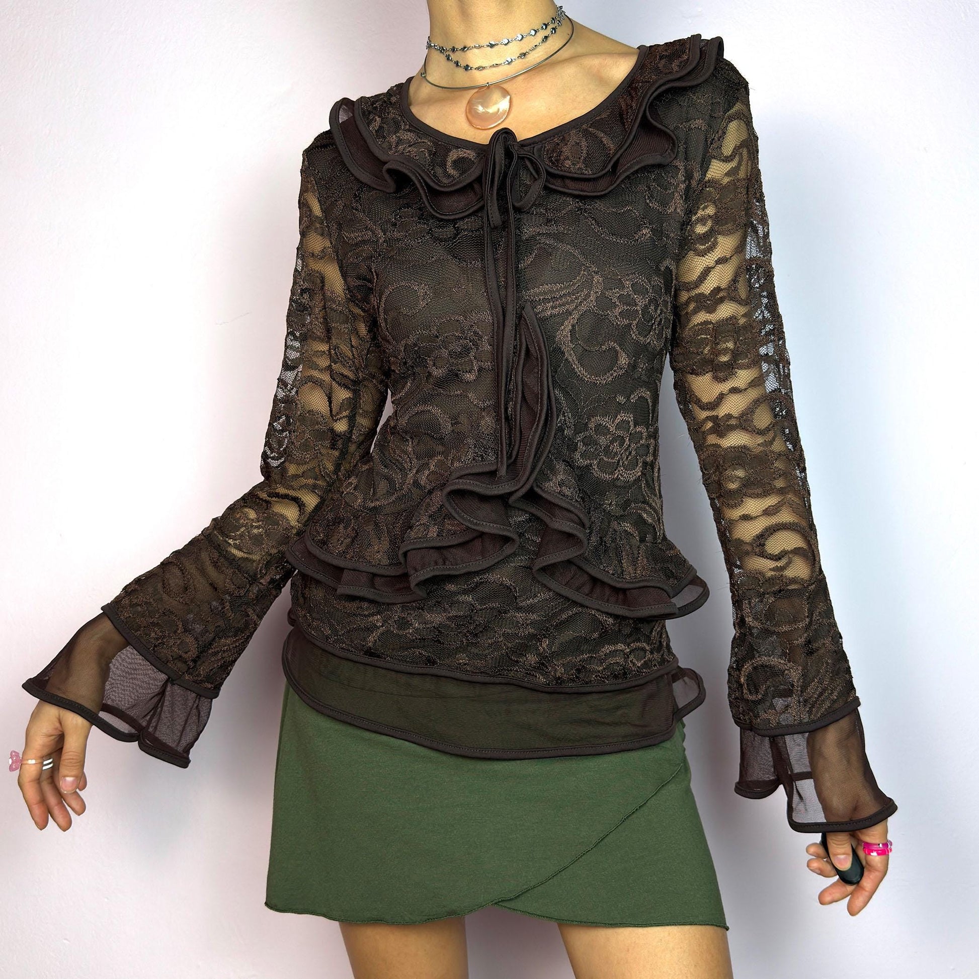 The Y2K Brown Lace Ruffle Top is a vintage 2000s statement piece, showcasing intricate floral lace throughout for a romantic and feminine look. This top features a stretchy semi-sheer fabric, layered ruffles along the neckline. adult world shop