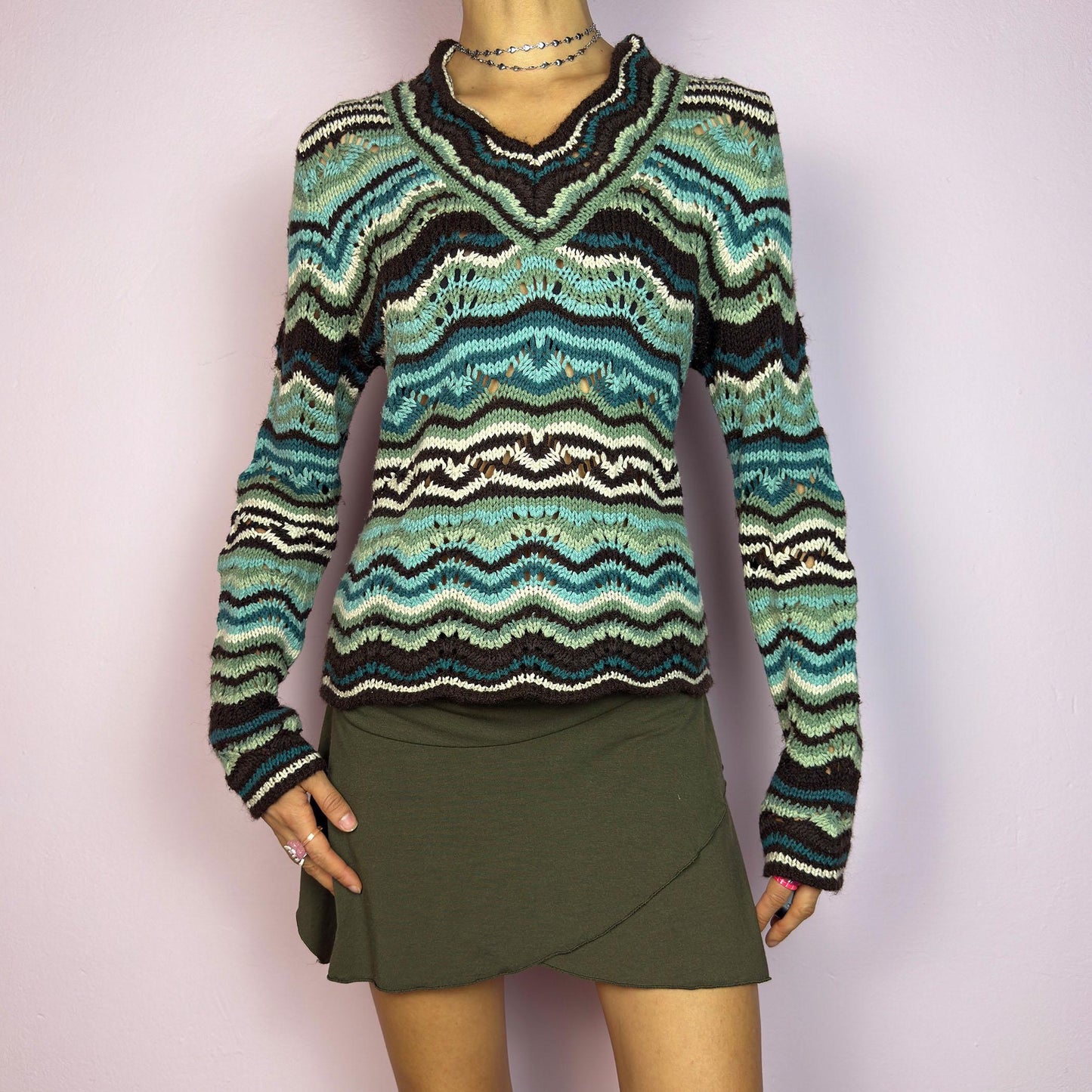 The Y2K Wave Open Knit Sweater is a vintage 2000s pullover featuring a mesmerizing wave-like pattern in shades of teal, brown and beige. This cozy sweater showcases a textured open-knit design, long sleeves, and a v-neckline. adult world shop