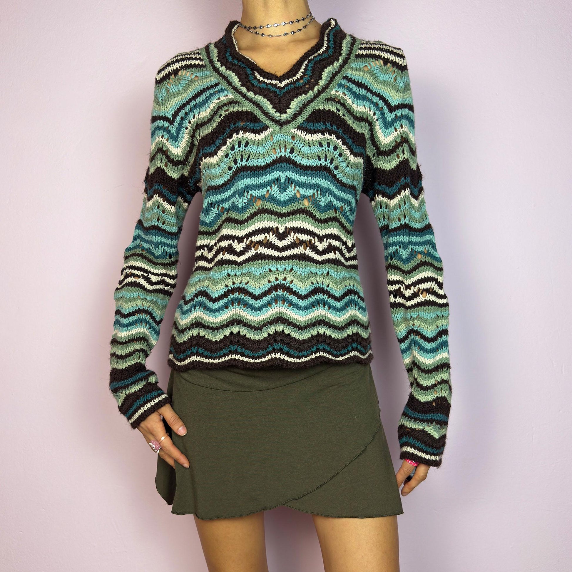 The Y2K Wave Open Knit Sweater is a vintage 2000s pullover featuring a mesmerizing wave-like pattern in shades of teal, brown and beige. This cozy sweater showcases a textured open-knit design, long sleeves, and a v-neckline. adult world shop