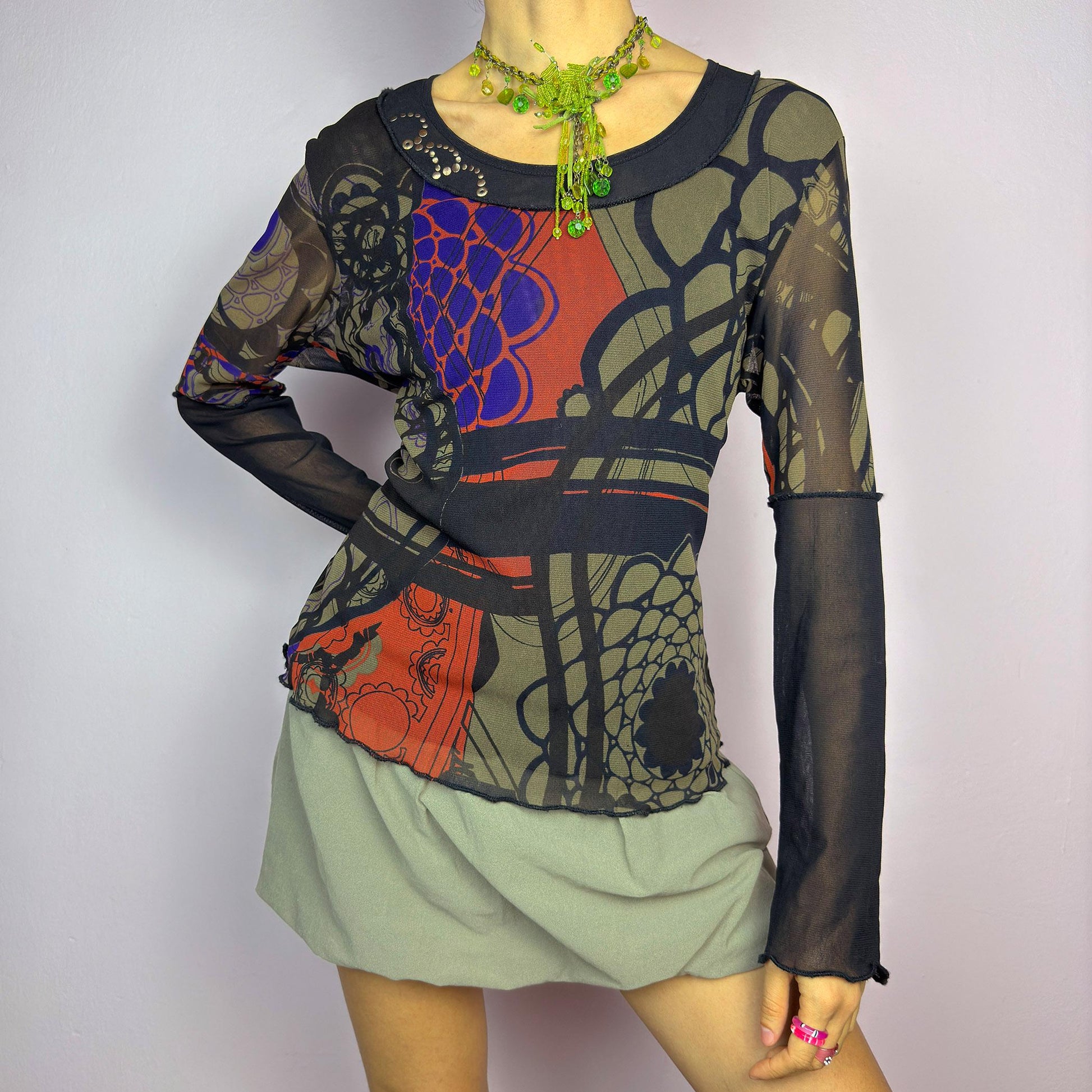 The Y2K Abstract Printed Mesh Top is a vintage 2000s sheer long-sleeve top featuring a bold abstract print in earthy tones with pops of red and blue. Designed with contrast black mesh sleeves, this artistic piece is perfect for edgy streetwear, cyberpunk, or grunge-inspired outfits. Ideal for layering or wearing solo for a statement look. adult world shop