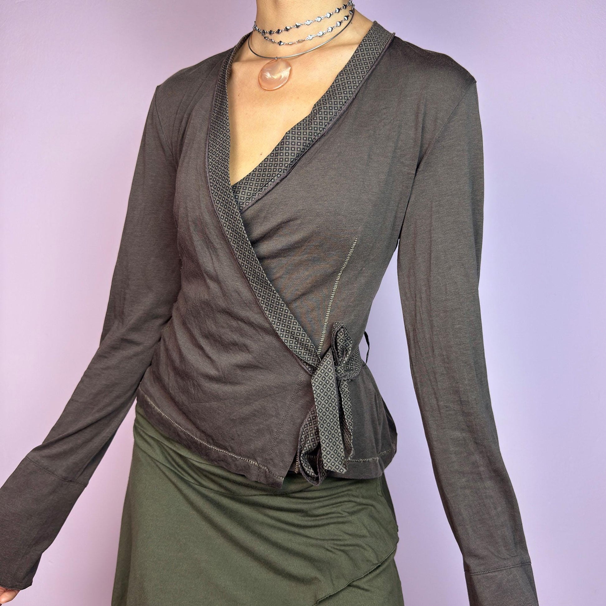 The Y2K Brown Wrap Cop Copine Top is a sleek and minimalist 2000s piece featuring a wrap-tie design with geometric-patterned trim details and flared cuffs. This top is crafted from a stretchy, comfortable fabric. adult world shop