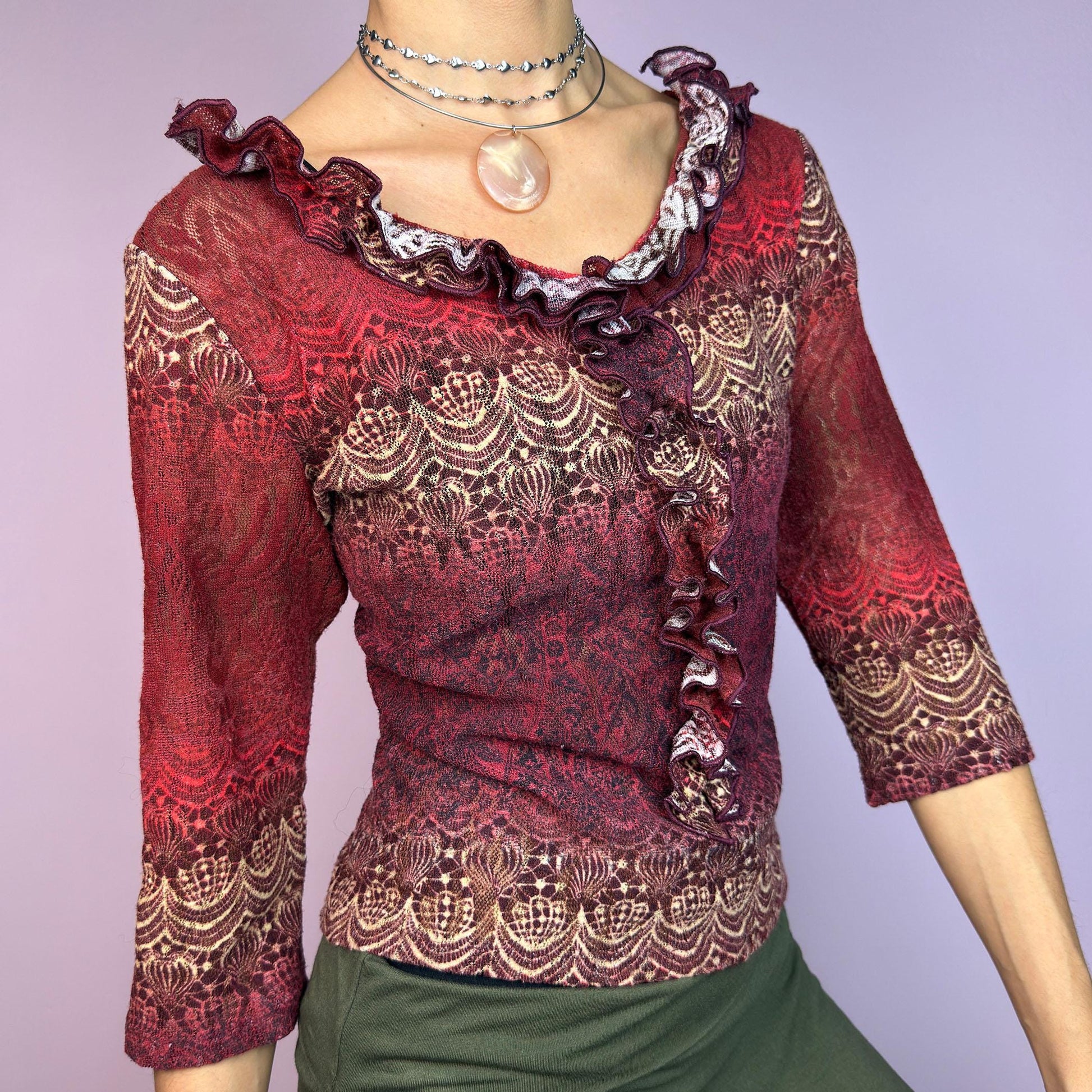 The Y2K Maroon Ruffle Mesh Top is a romantic vintage 2000s piece. Featuring a semi-sheer lace-inspired design in warm red tones, it showcases intricate patterns complemented by a ruffled neckline and 3/4 sleeves. adult world shop