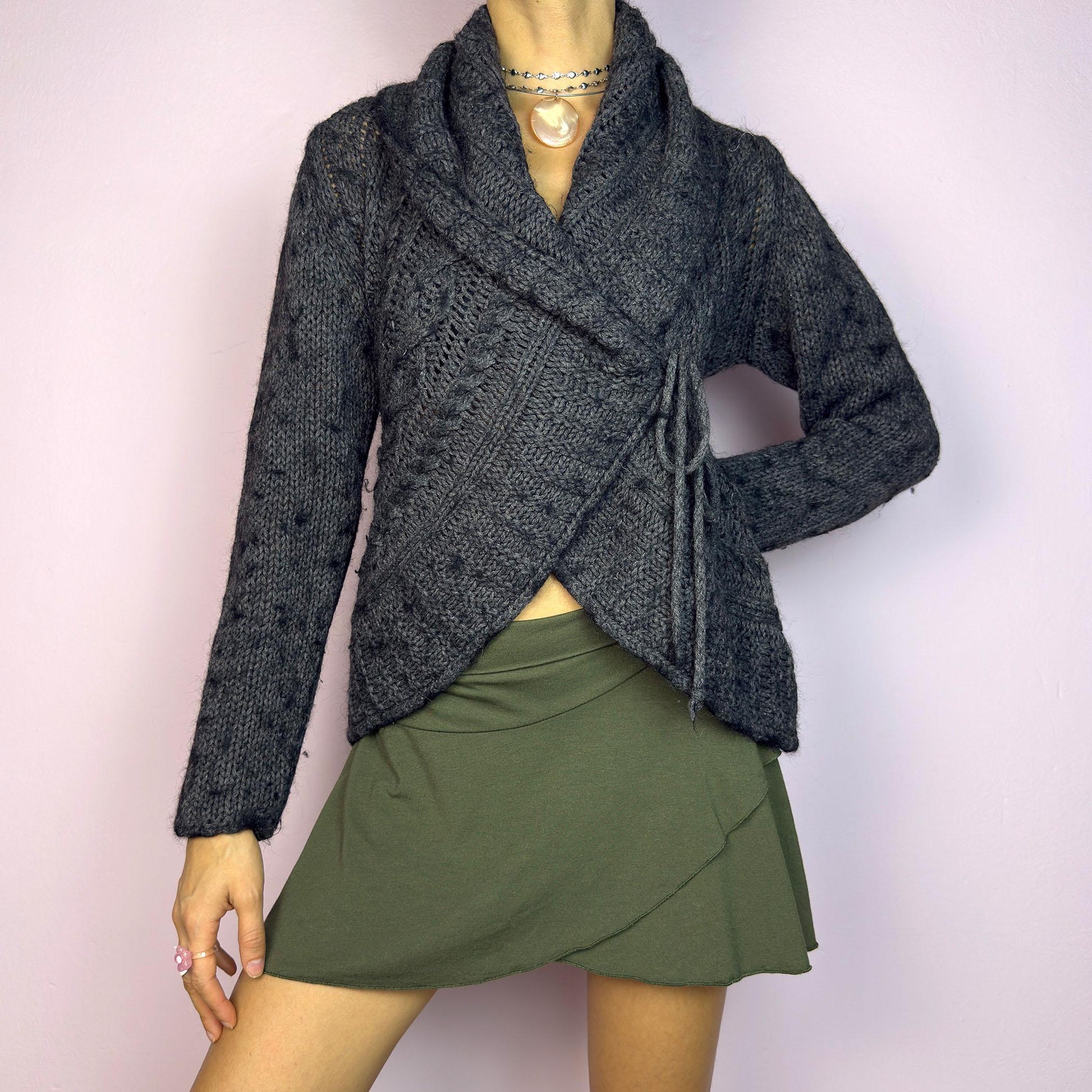 The Y2K Gray Wrap Tie Cardigan is a cozy vintage 2000s piece. This dark gray cardigan features a chunky knit design with intricate cable-knit detailing and a wrap-front closure that ties at the side for an adjustable fit. adult world shop