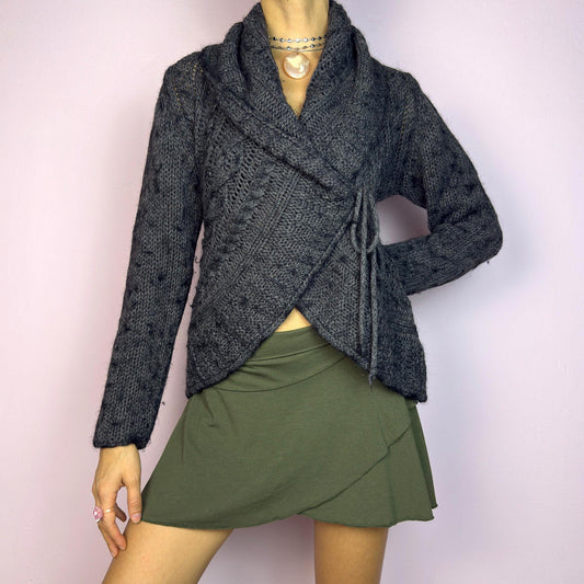 The Y2K Gray Wrap Tie Cardigan is a cozy vintage 2000s piece. This dark gray cardigan features a chunky knit design with intricate cable-knit detailing and a wrap-front closure that ties at the side for an adjustable fit. adult world shop