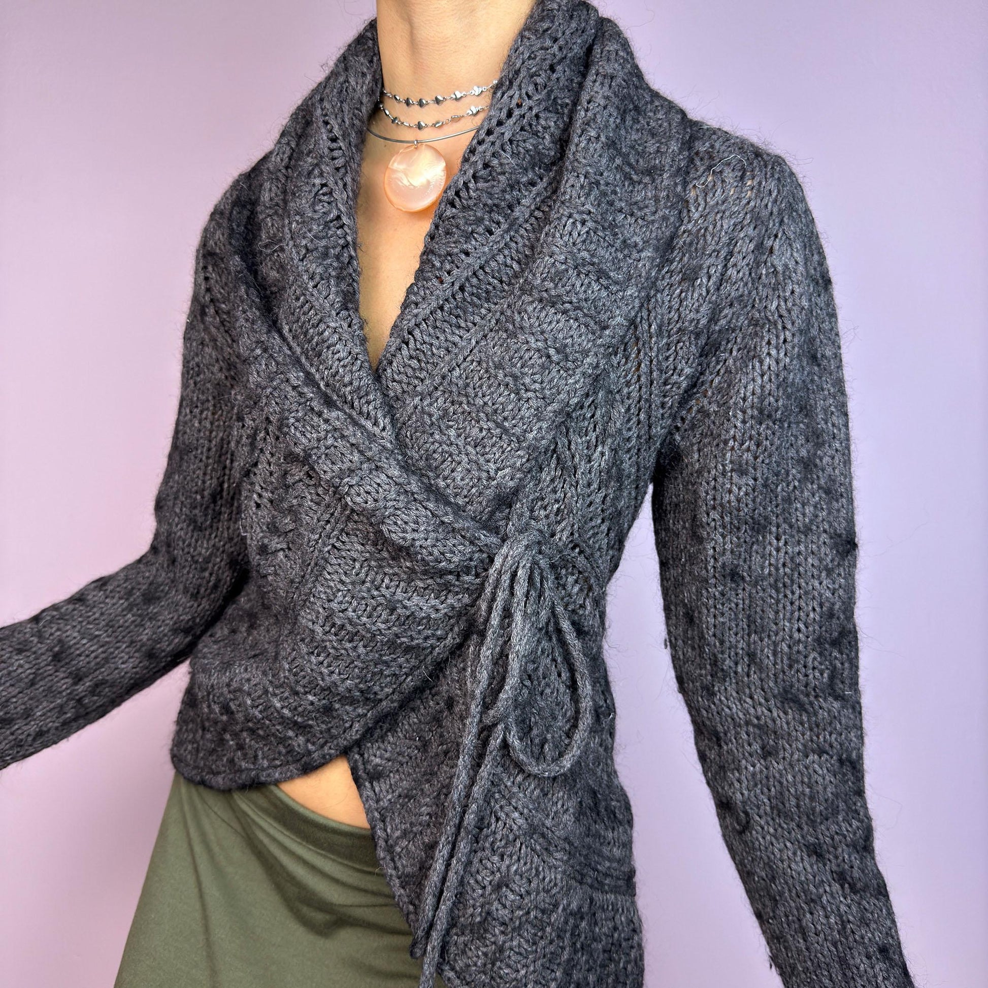 The Y2K Gray Wrap Tie Cardigan is a cozy vintage 2000s piece. This dark gray cardigan features a chunky knit design with intricate cable-knit detailing and a wrap-front closure that ties at the side for an adjustable fit. adult world shop