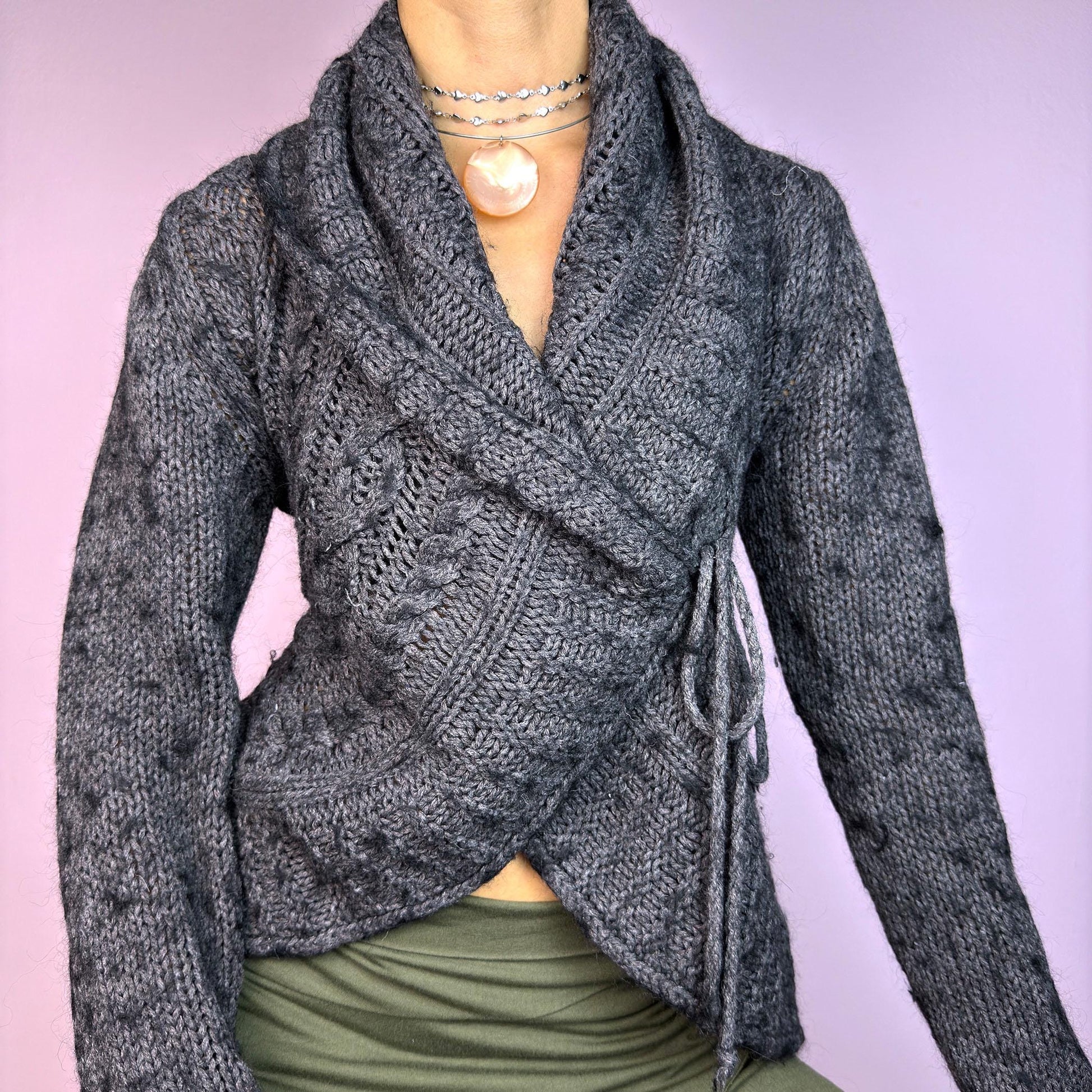 The Y2K Gray Wrap Tie Cardigan is a cozy vintage 2000s piece. This dark gray cardigan features a chunky knit design with intricate cable-knit detailing and a wrap-front closure that ties at the side for an adjustable fit. adult world shop