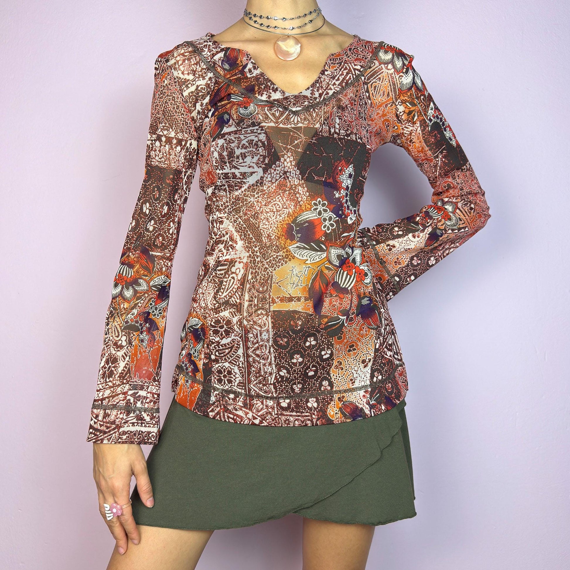 The Y2K Mesh Flared Long Sleeve Top is a vibrant vintage 2000s piece, featuring a floral and paisley print in earthy tones of orange, red, and brown. Crafted from lightweight mesh fabric, this top has a semi-sheer finish. adult world shop