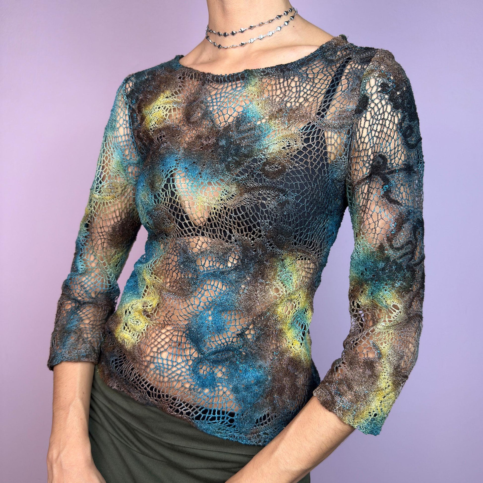 The Y2K Open Knit Mesh Top is a unique vintage 2000s piece featuring an intricate open-knit design, this semi-sheer top boasts a dreamy tie-dye-inspired blend of earthy hues in brown, blue and green. adult world shop