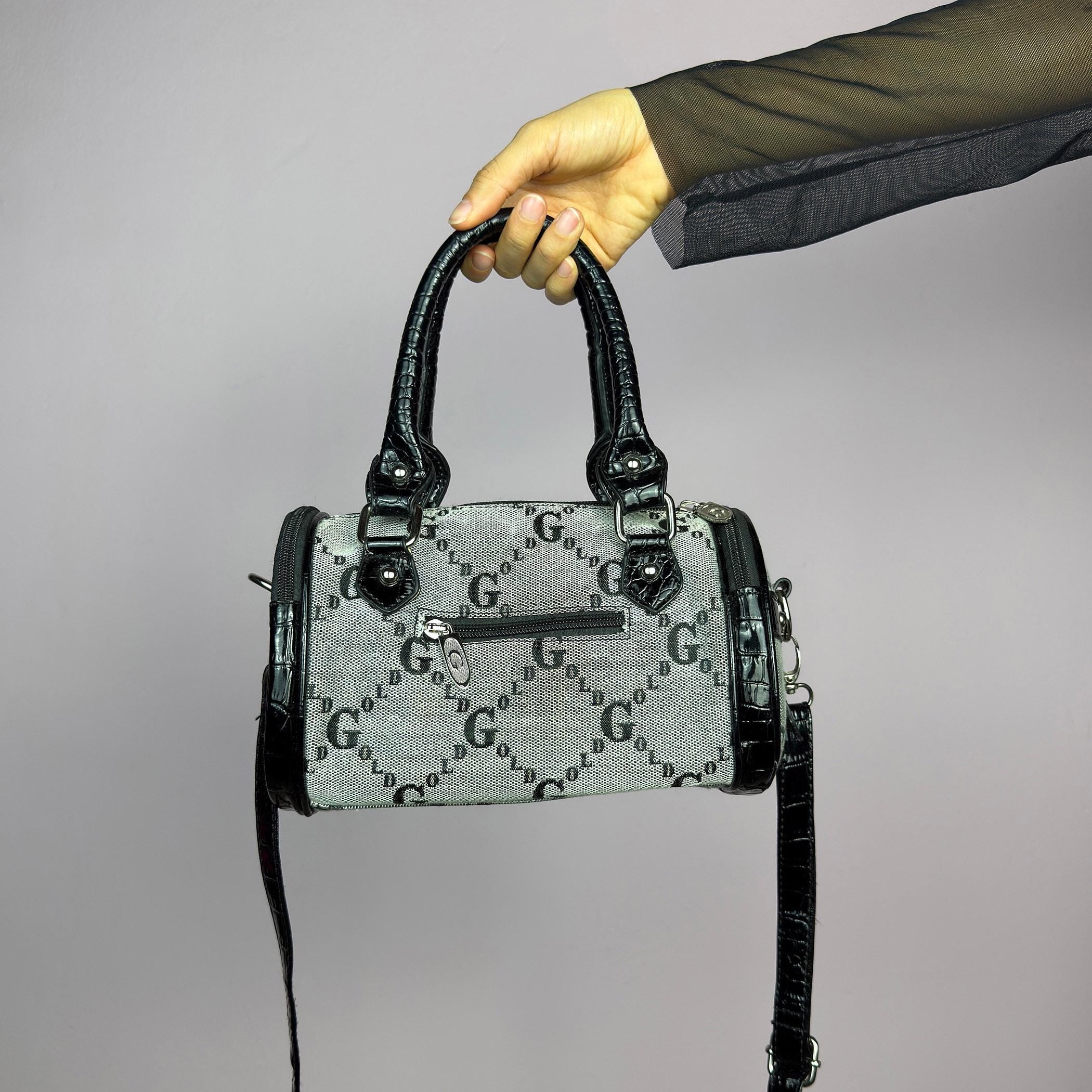 The Y2K Monogram Mini Duffel Bag is a stylish vintage 2000s accessory. Featuring a structured silhouette with an all-over monogram print, sleek black faux patent leather accents, and silver hardware. It includes dual top handles. adult world shop