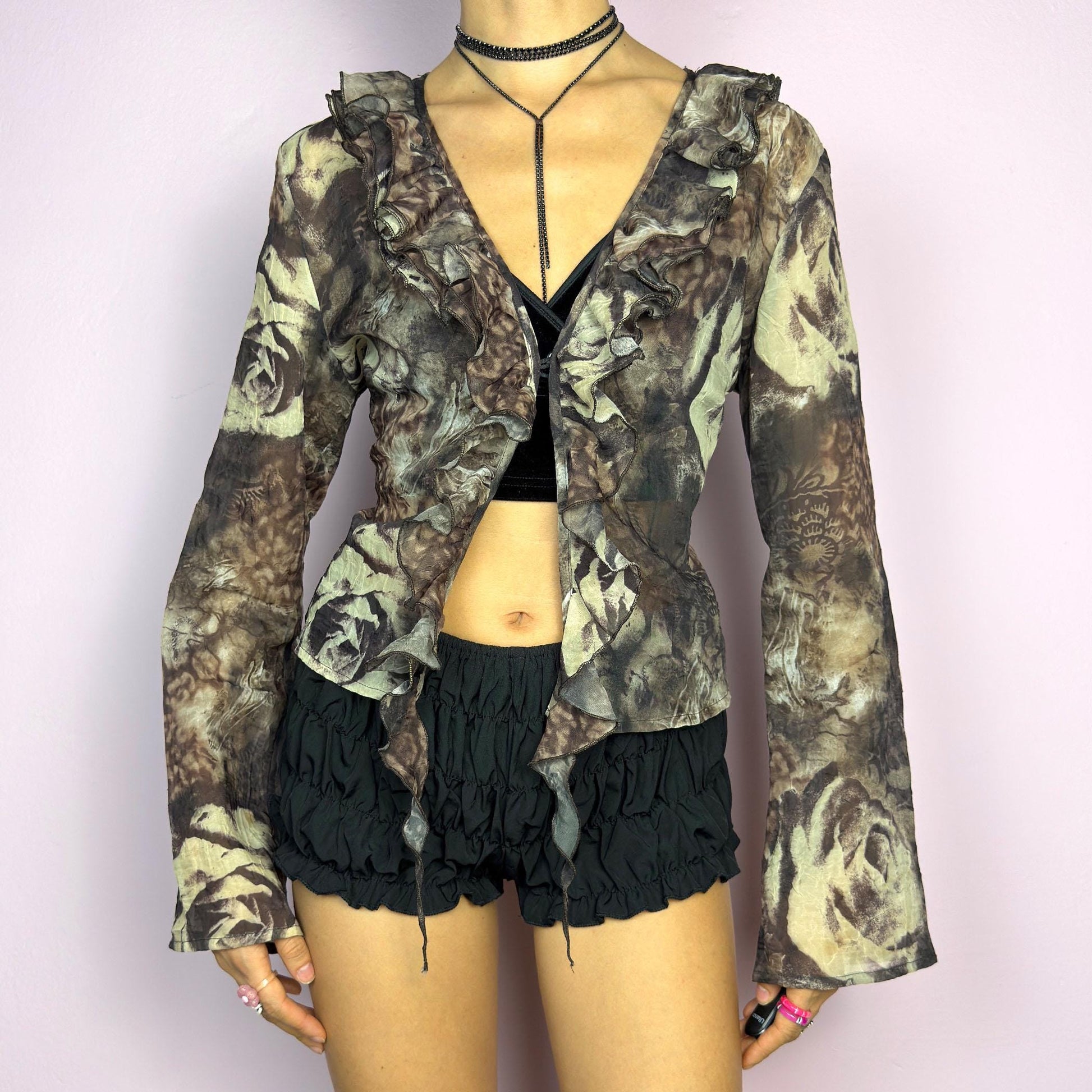 The Y2K Printed Ruffle Blouse is a stunning vintage 2000s romantic piece crafted from sheer, lightweight fabric in brown tones and featuring a blend of earthy hues in a rose-patterned print. adult world shop