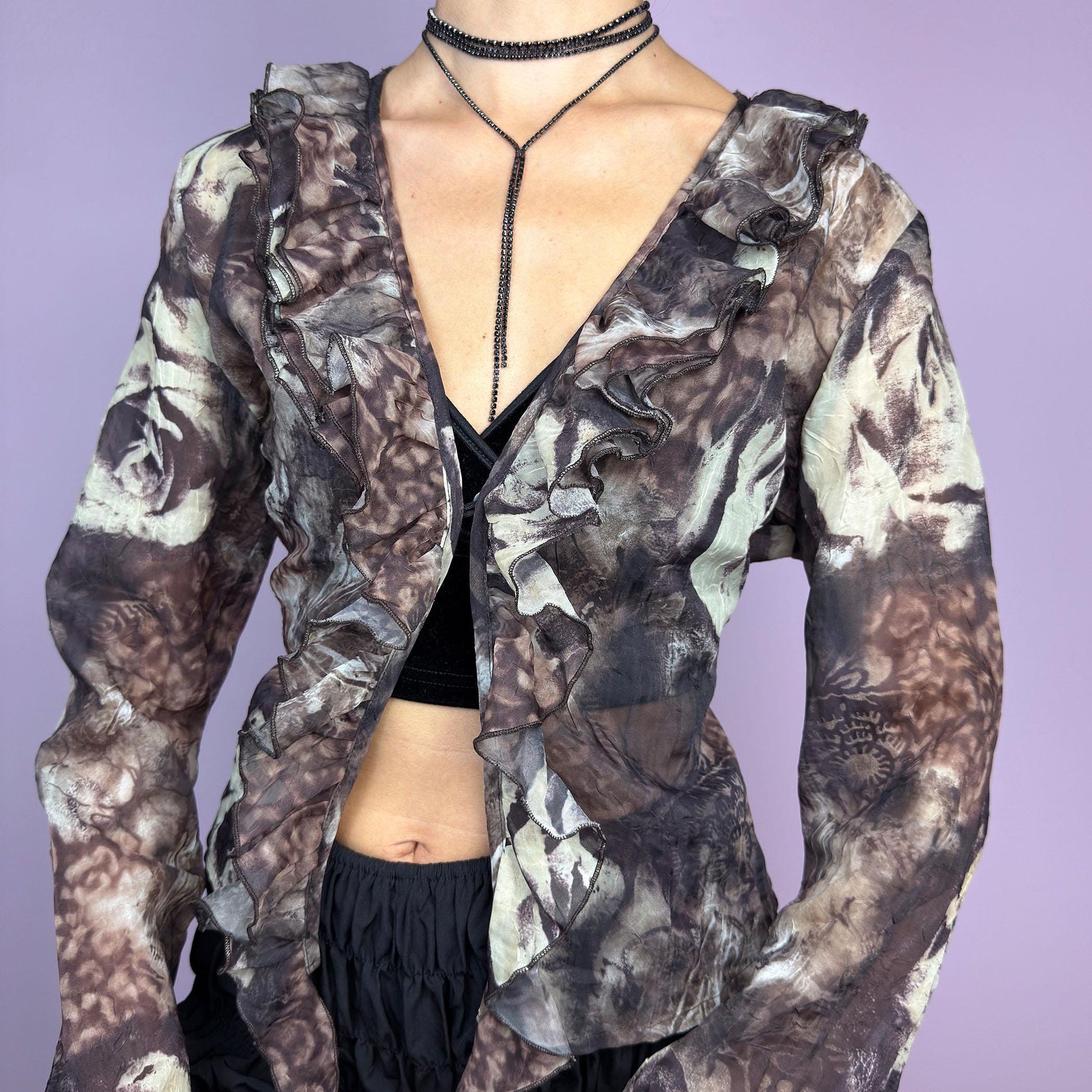 The Y2K Printed Ruffle Blouse is a stunning vintage 2000s romantic piece crafted from sheer, lightweight fabric in brown tones and featuring a blend of earthy hues in a rose-patterned print. adult world shop