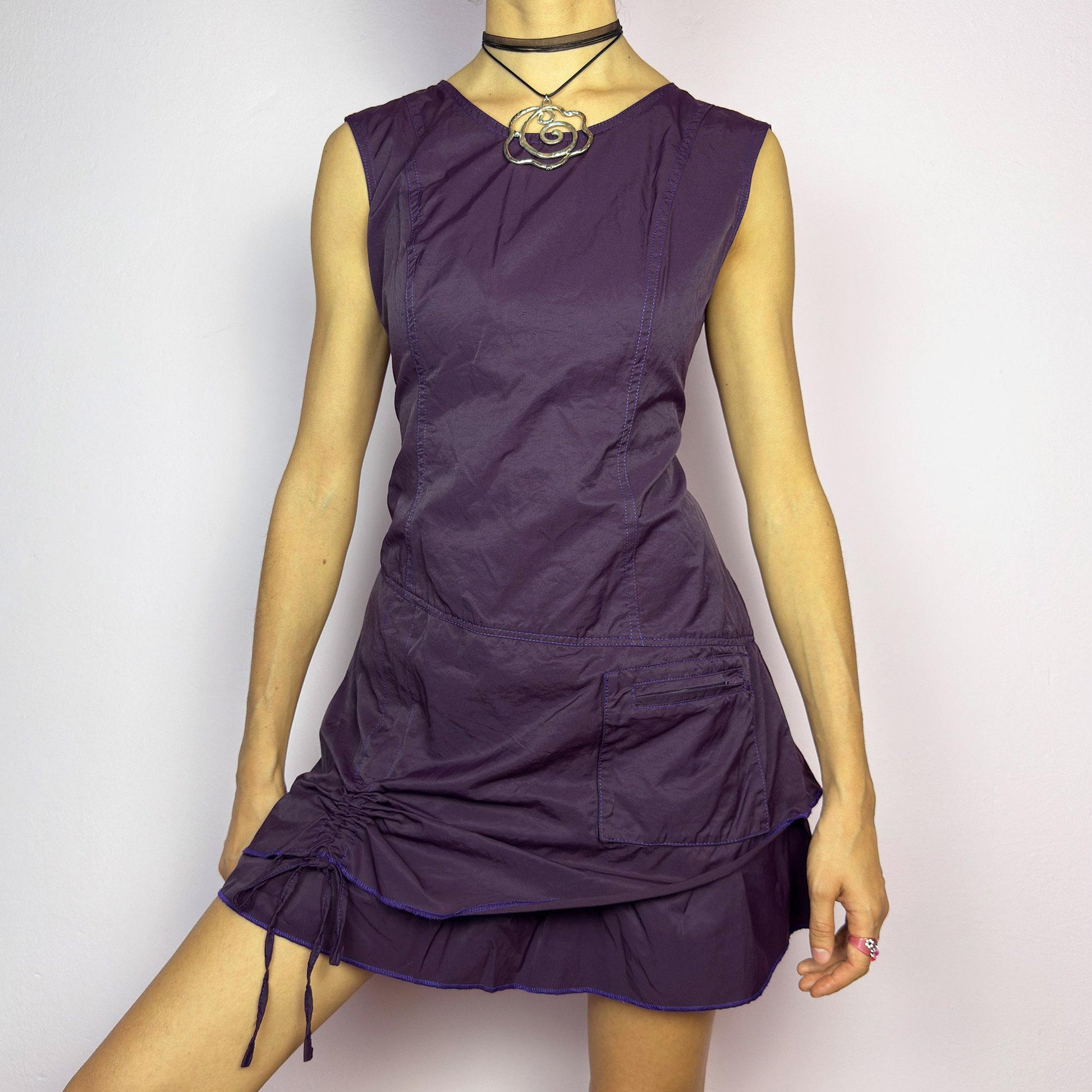 The Y2K Purple Layered Mini Dress is a vintage 2000s sleeveless dress in a deep purple hue, featuring a structured, layered silhouette, a side pocket, an adjustable drawstring ruched detail on the side for a customizable fit. adult world shop
