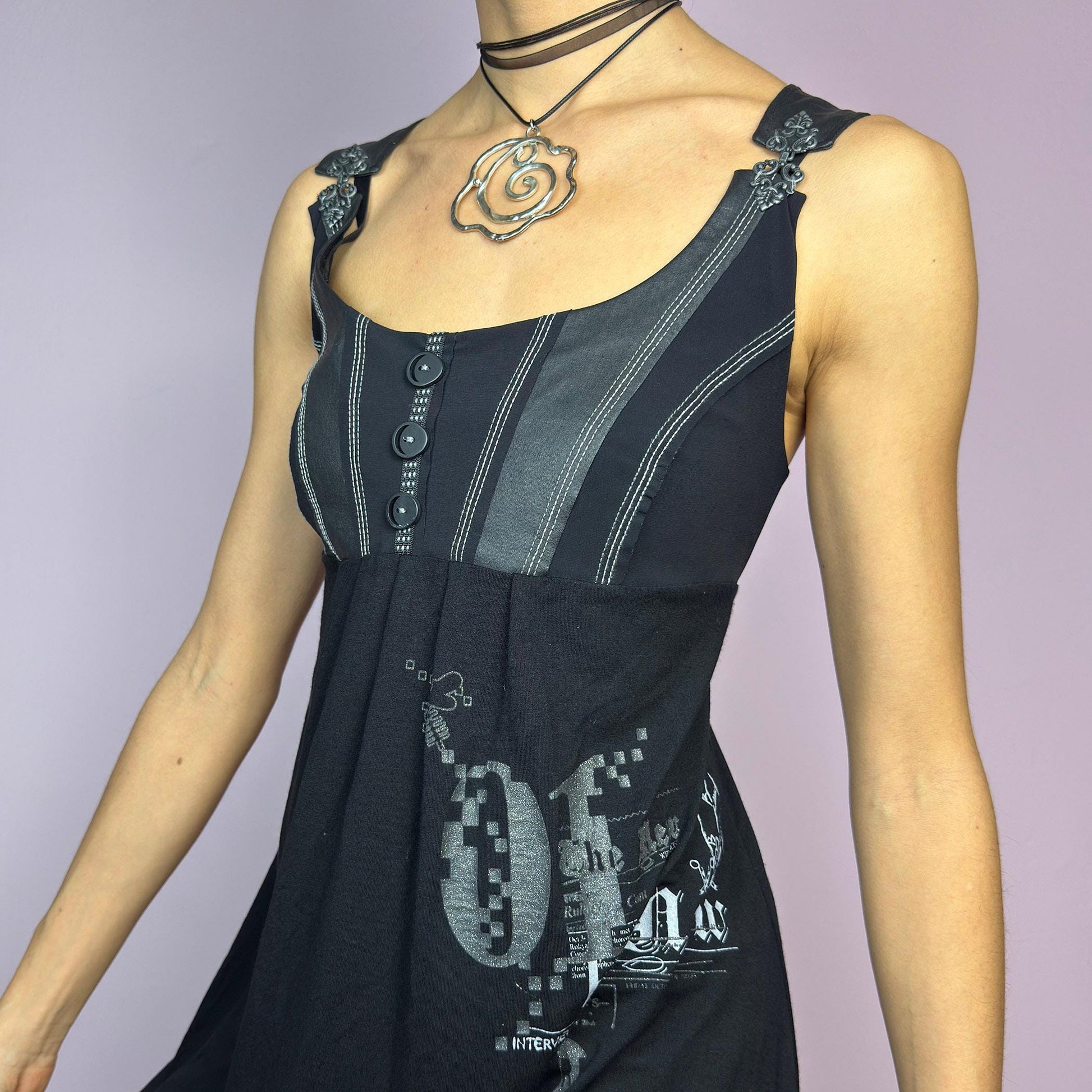 The Y2K Black Buckle Strap Mini Dress is a vintage 2000s sleeveless piece with a mix of edgy and casual aesthetics. It features decorative button details, contrast stitching, and graphic prints. adult world shop
