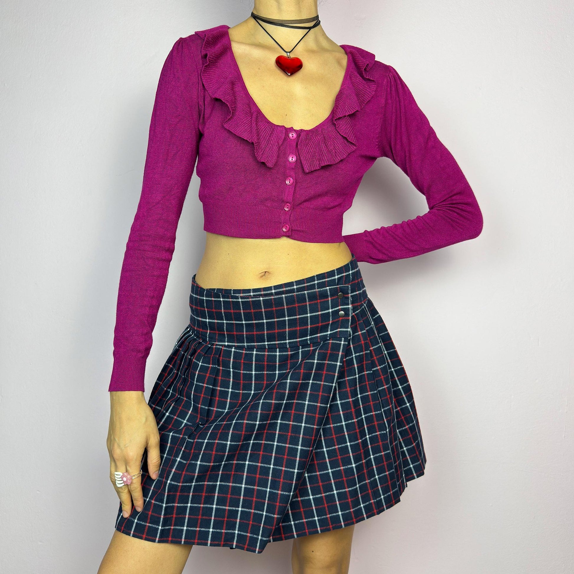 The Y2K Plaid Pleated Wrap Mini Skirt is a vintage 2000s piece featuring a wrap-style waistband with snap button details. Made from a plaid fabric in navy blue tones, it has structured pleats that create a classic silhouette. adult world shop