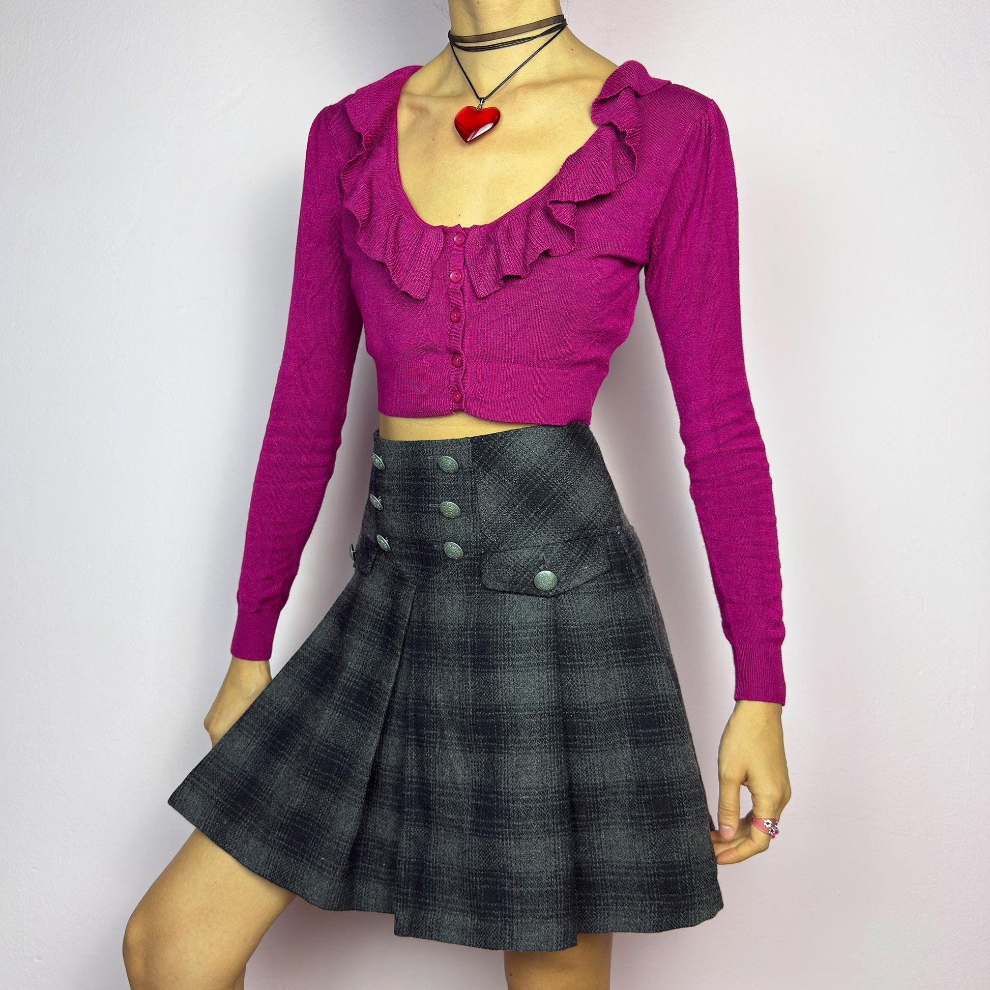 The Y2K Gray Plaid Pleated Mini Skirt is a vintage 2000s essential, featuring a structured pleated design with decorative button details. Made from a thick woven fabric with a black plaid pattern, it is ideal for winter outfits. adult world shop