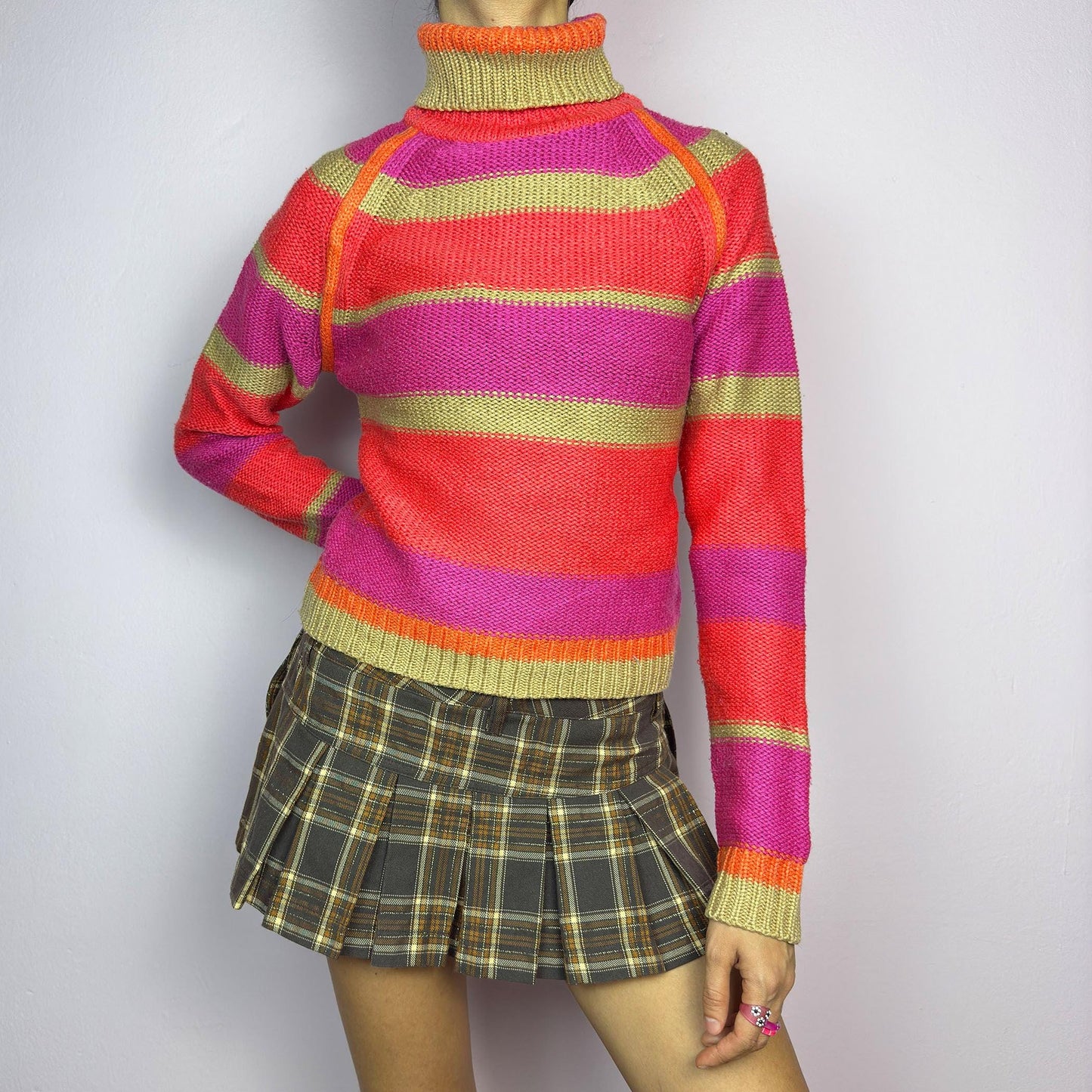 The Y2K Turtleneck Striped Sweater is a vintage 2000s staple featuring a bold striped design in vibrant tones. Crafted from a knit fabric, it has a cozy ribbed turtleneck, cuffs, and hem for a snug fit. adult world shop
