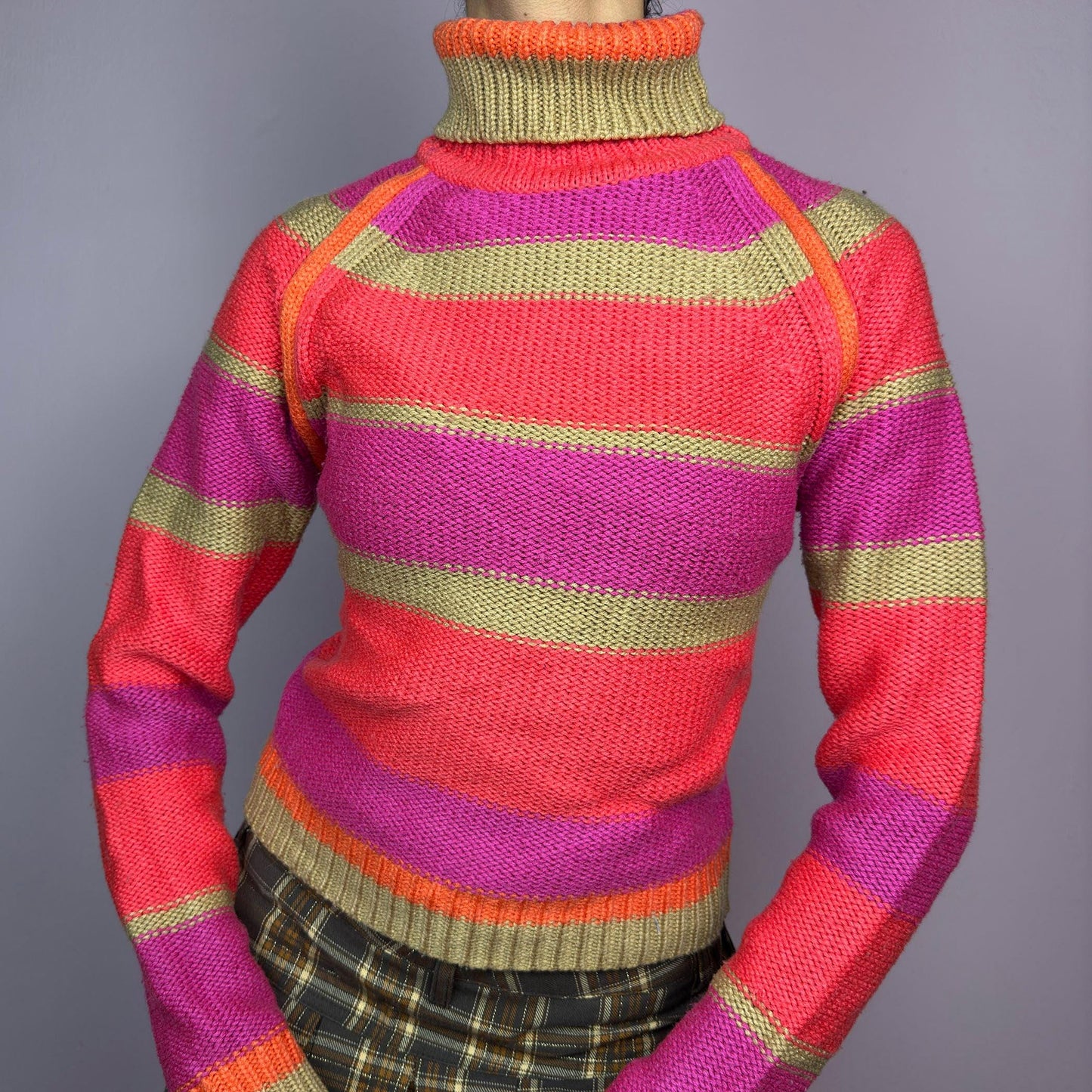 The Y2K Turtleneck Striped Sweater is a vintage 2000s staple featuring a bold striped design in vibrant tones. Crafted from a knit fabric, it has a cozy ribbed turtleneck, cuffs, and hem for a snug fit. adult world shop