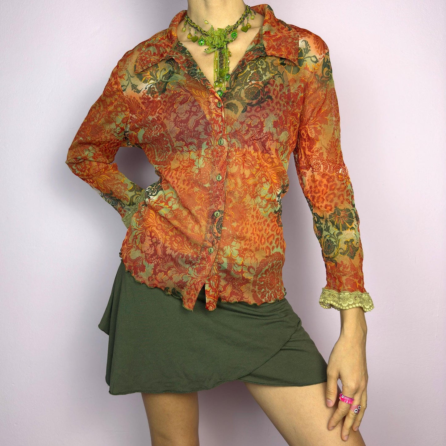 The Y2K Baroque Print Mesh Blouse is a vintage 2000s piece featuring a semi-sheer mesh fabric with a rich baroque-inspired floral print in warm tones. Designed with a fitted silhouette, button-up front, delicate lace trim on the cuffs and three quarter sleeves, the lightweight and stretchy fabric make it ideal for summer bohemian-inspired looks. adult world shop