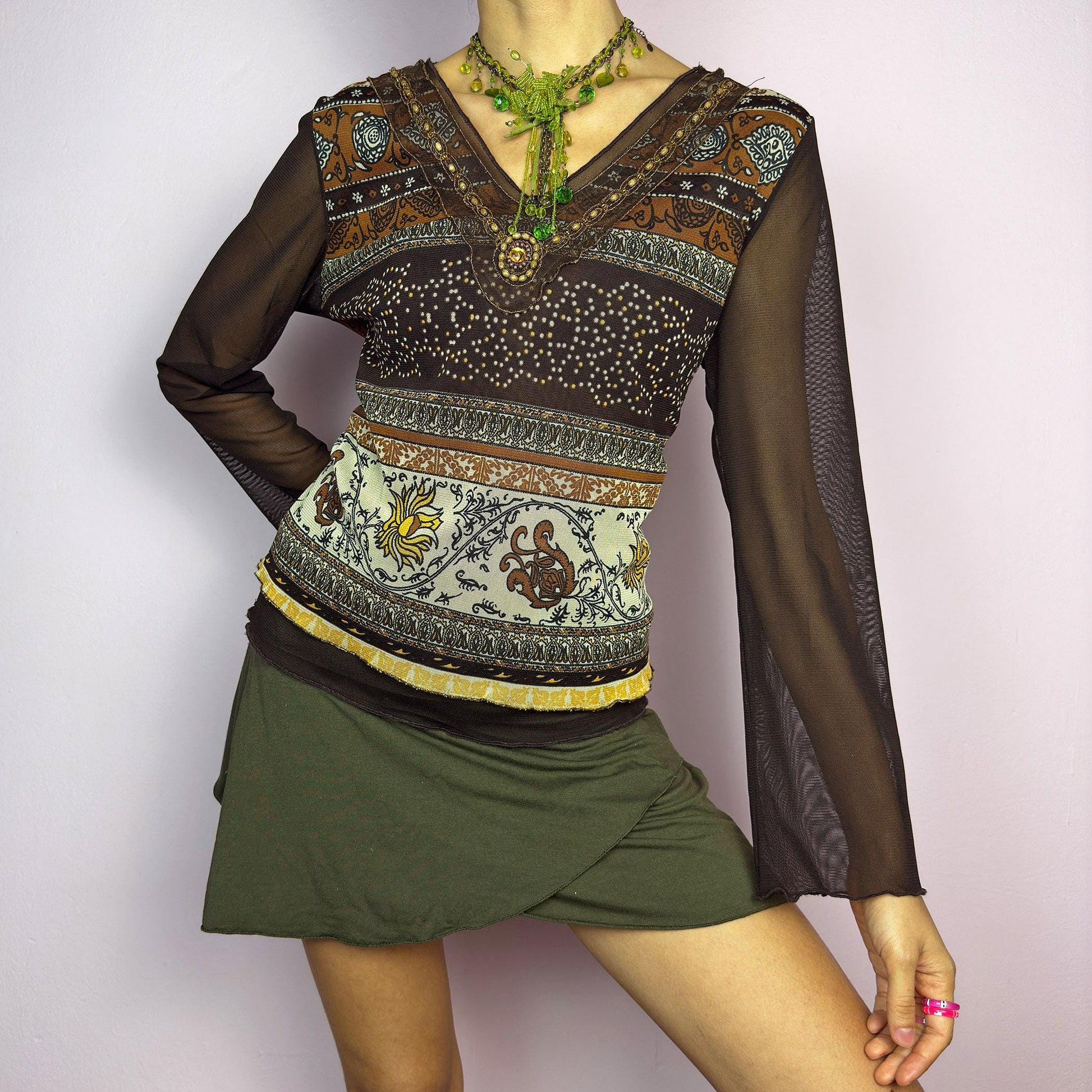 The Y2K Brown Bell Sleeve Mesh Top is a vintage 2000s piece featuring a semi-sheer mesh fabric with baroque and floral-inspired prints. Designed with flared bell sleeves, a fitted silhouette, and a layered hem, this top embodies a dreamy bohemian aesthetic. The lightweight and stretchy fabric make it perfect for ethereal, fairy-grunge looks. adult world shop