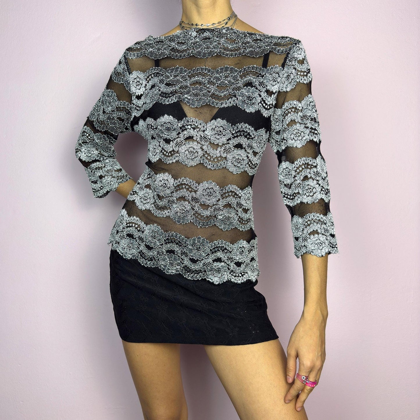 The Y2K Lace Mesh Black Top is a vintage 2000s statement sheer blouse featuring a delicate black mesh base with intricate silver lace embroidery in horizontal stripes. Designed with a fitted silhouette and three-quarter sleeves, this top is perfect for a romantic night or a bold evening outfit.