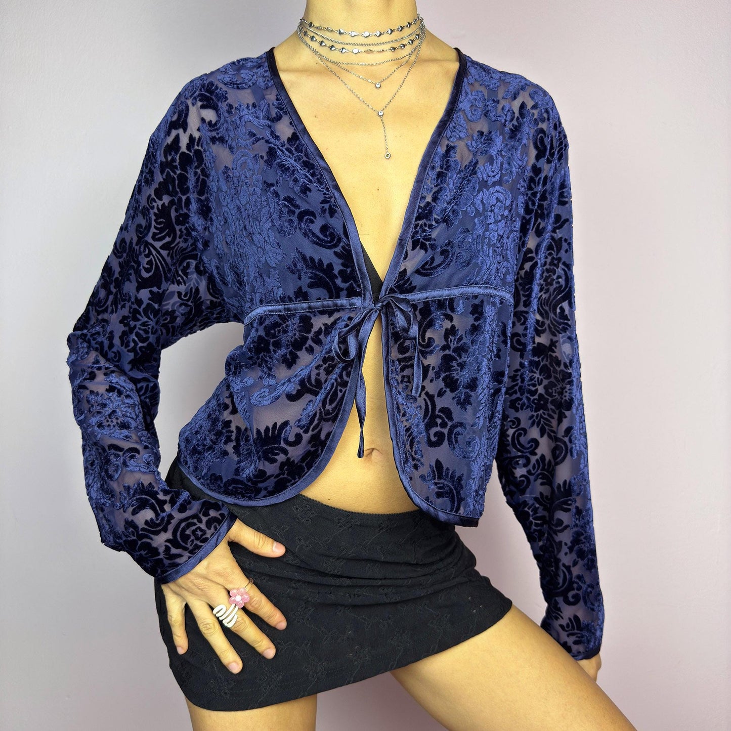 The Vintage 90s Blue Velvet Sheer Blouse is a romantic sheer velvet top featuring a flocked baroque floral pattern on deep navy blue. Designed with a plunging V-neckline, long sleeves, and a delicate tie-front closure, this blouse is perfect for night-out looks. adult world shop