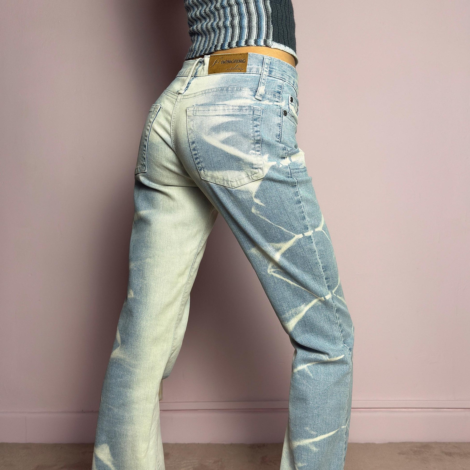 The Y2K Bleached Flare Jeans are a vintage 2000s statement piece featuring a light-wash denim with a bold bleached abstract pattern for a deconstructed, experimental look. Designed with a flattering mid-rise fit, flared legs, button and zipper closure, and pockets, these jeans are a perfect blend of edgy and playful aesthetics. Ideal for standout casual outfits. adult world shop