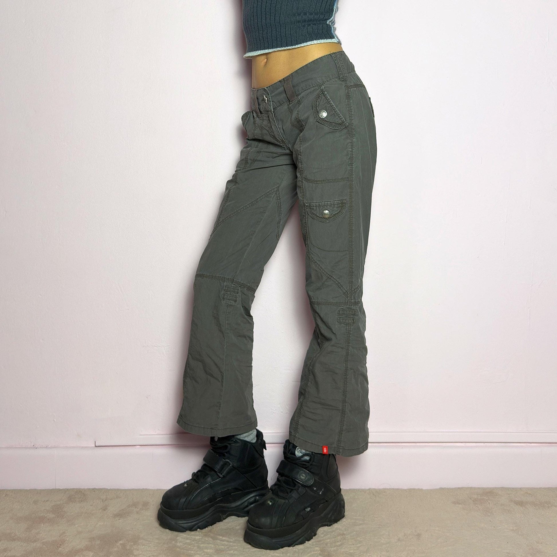 The Y2K Low-Rise Cargo Pants are a vintage 2000s piece featuring a washed gray tone with contrast stitching. Designed with a low-rise fit, button and zipper closure, and multiple cargo-style pockets, these pants have panel detailing and exposed seams that enhance their utilitarian aesthetic. The cropped straight-leg cut adds a modern touch, making them perfect for grunge and streetwear-inspired outfits. adult world shop
