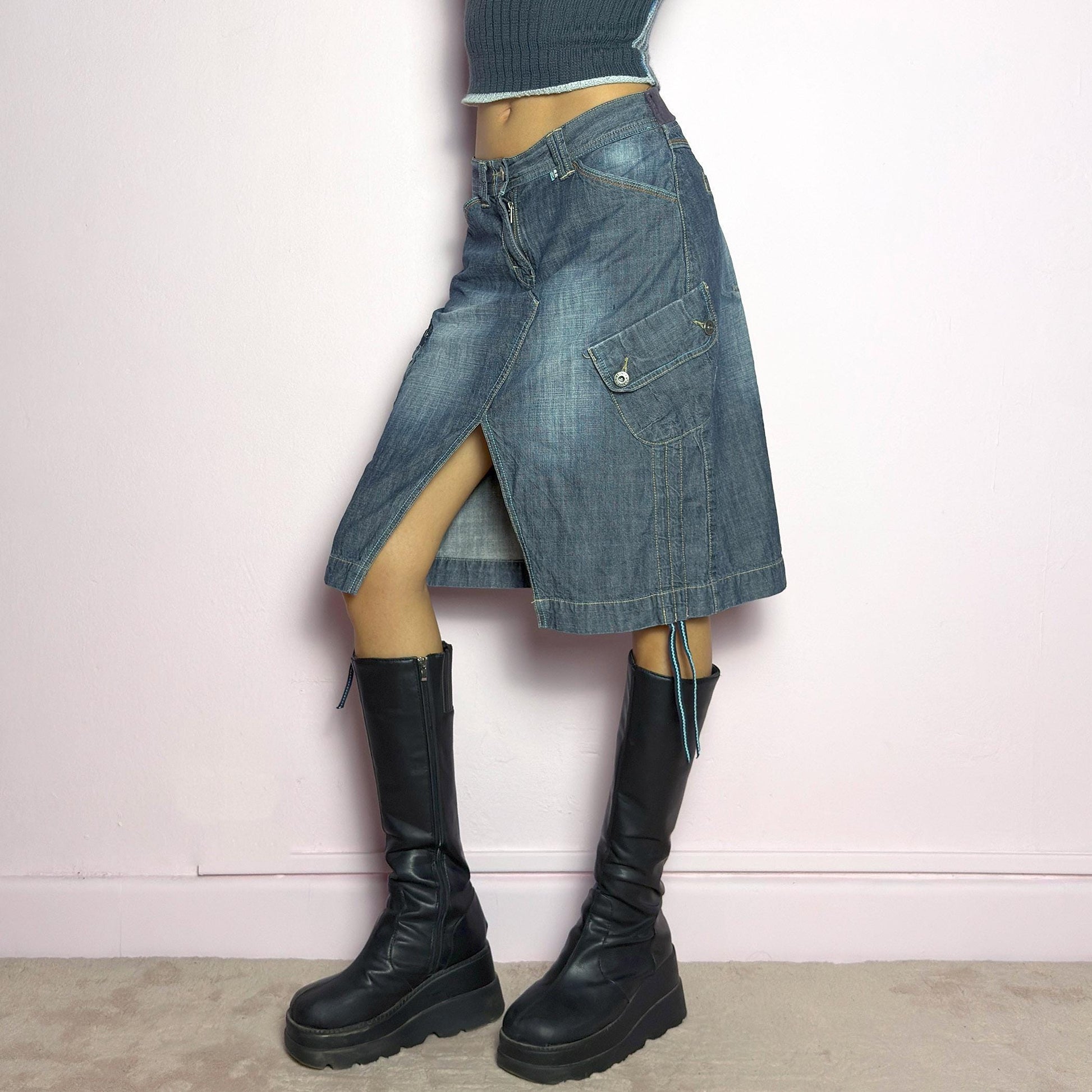 The Y2K Deconstructed Denim Midi Skirt is a vintage 2000s standout piece featuring a structured dark-wash denim fabric with contrast stitching. Designed with an asymmetrical front slit, utility-style cargo pockets, and adjustable drawstrings. Finished with a button and zipper closure, belt loops, and a mid-length silhouette, it&#39;s perfect for effortless grunge and utilitarian-inspired outfits. adult world shop