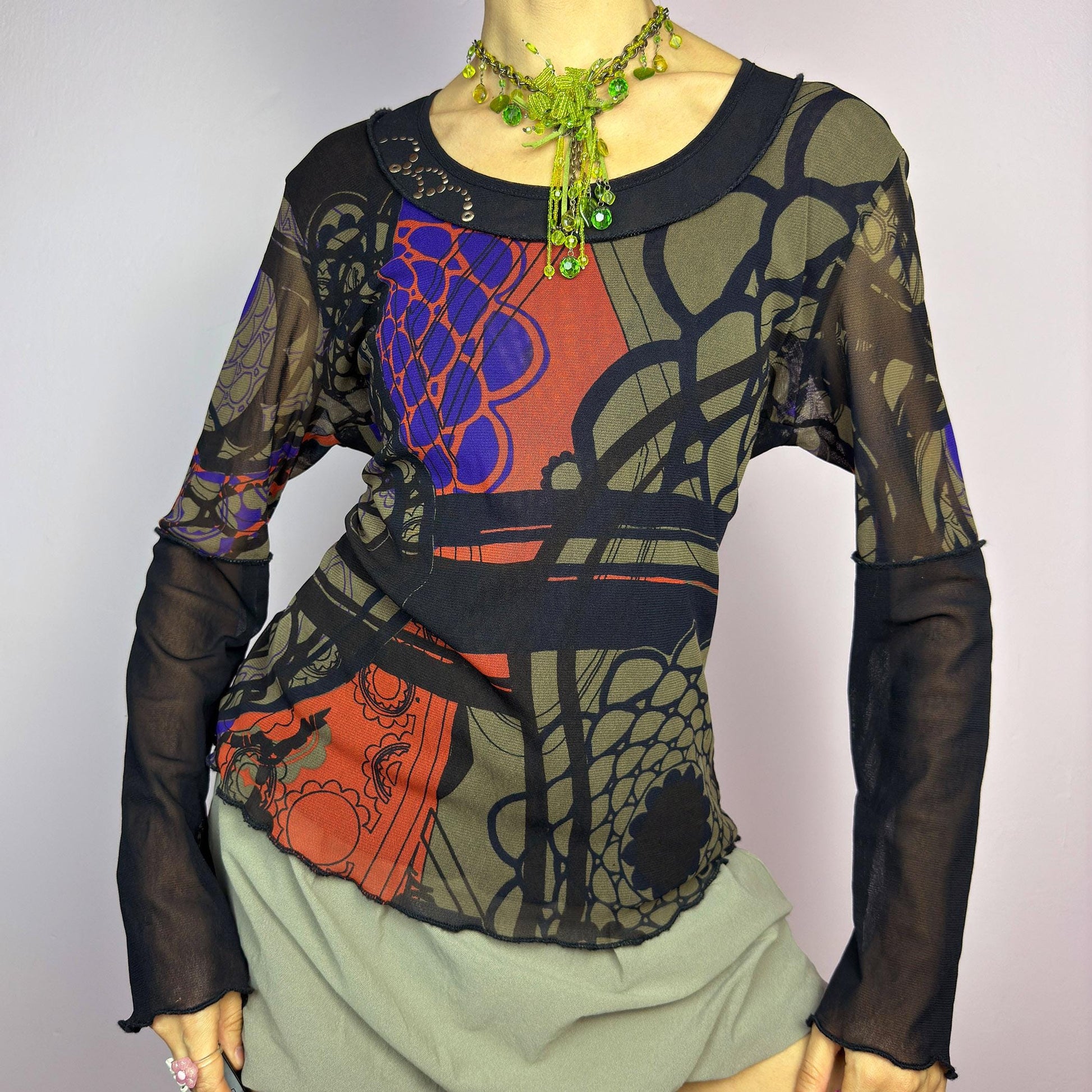 The Y2K Abstract Printed Mesh Top is a vintage 2000s sheer long-sleeve top featuring a bold abstract print in earthy tones with pops of red and blue. Designed with contrast black mesh sleeves, this artistic piece is perfect for edgy streetwear, cyberpunk, or grunge-inspired outfits. Ideal for layering or wearing solo for a statement look. adult world shop