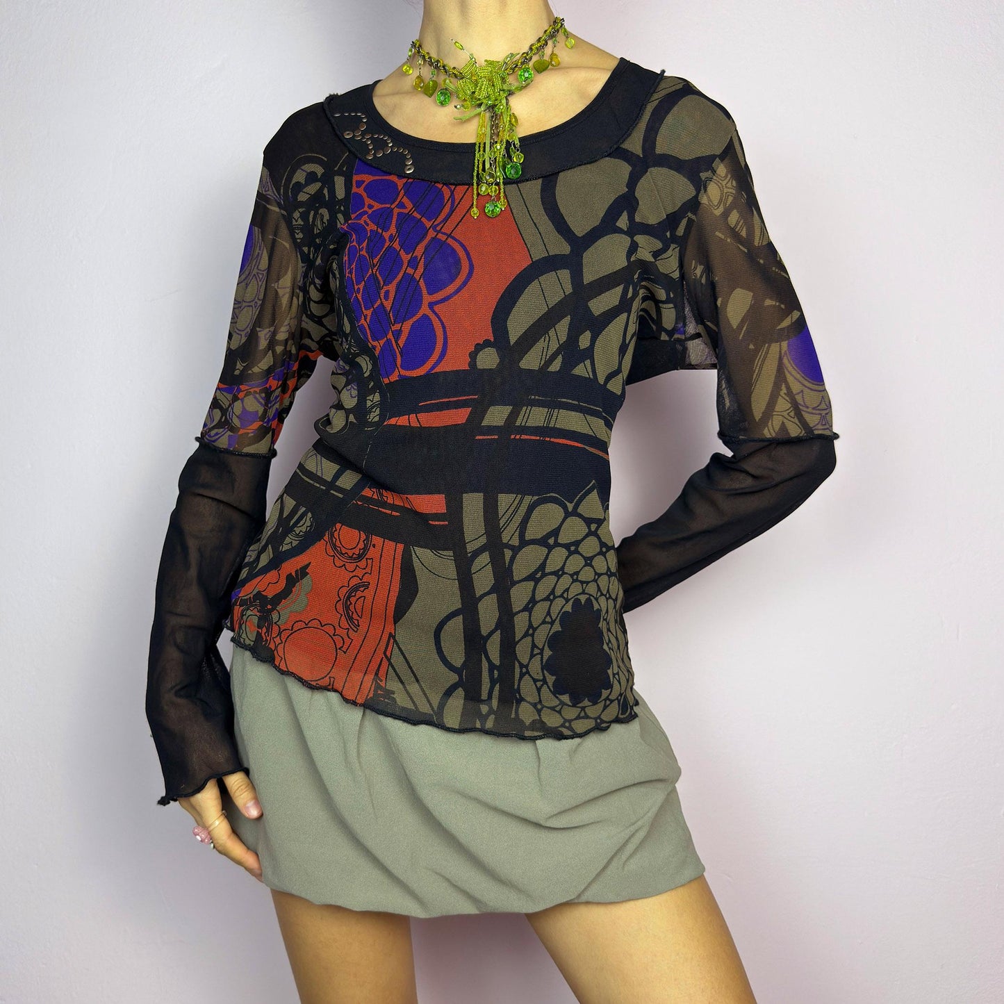 The Y2K Abstract Printed Mesh Top is a vintage 2000s sheer long-sleeve top featuring a bold abstract print in earthy tones with pops of red and blue. Designed with contrast black mesh sleeves, this artistic piece is perfect for edgy streetwear, cyberpunk, or grunge-inspired outfits. Ideal for layering or wearing solo for a statement look. adult world shop
