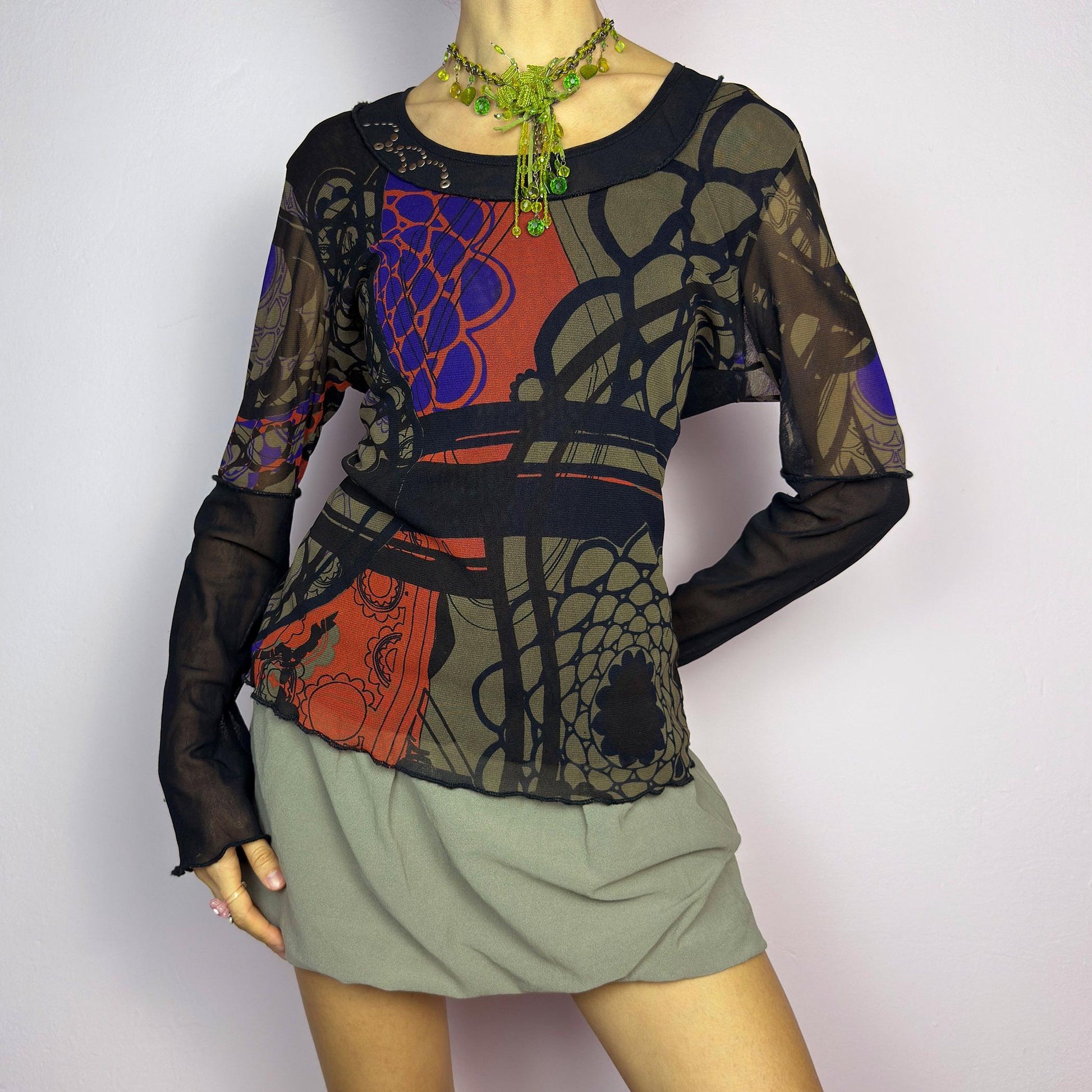 The Y2K Abstract Printed Mesh Top is a vintage 2000s sheer long-sleeve top featuring a bold abstract print in earthy tones with pops of red and blue. Designed with contrast black mesh sleeves, this artistic piece is perfect for edgy streetwear, cyberpunk, or grunge-inspired outfits. Ideal for layering or wearing solo for a statement look. adult world shop