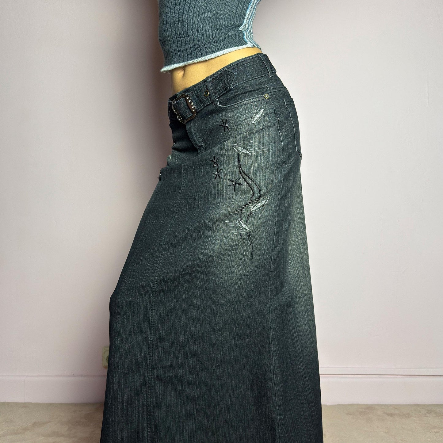 The Y2K Black Denim Maxi Skirt is a vintage 2000s piece featuring a sleek dark wash, rhinestone embellishments, and contrast stitching. Designed with a mid-rise fit and a stretchy denim fabric, it offers a structured silhouette that flares at the bottom. The skirt is finished with a button and zipper closure, pockets, and a removable belt for a customizable look. Perfect for casual streetwear outfits or an elegant night out. adult world shop
