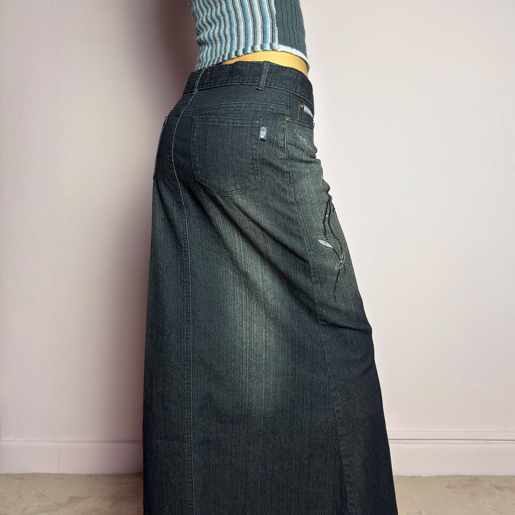 The Y2K Black Denim Maxi Skirt is a vintage 2000s piece featuring a sleek dark wash, rhinestone embellishments, and contrast stitching. Designed with a mid-rise fit and a stretchy denim fabric, it offers a structured silhouette that flares at the bottom. The skirt is finished with a button and zipper closure, pockets, and a removable belt for a customizable look. Perfect for casual streetwear outfits or an elegant night out. adult world shop